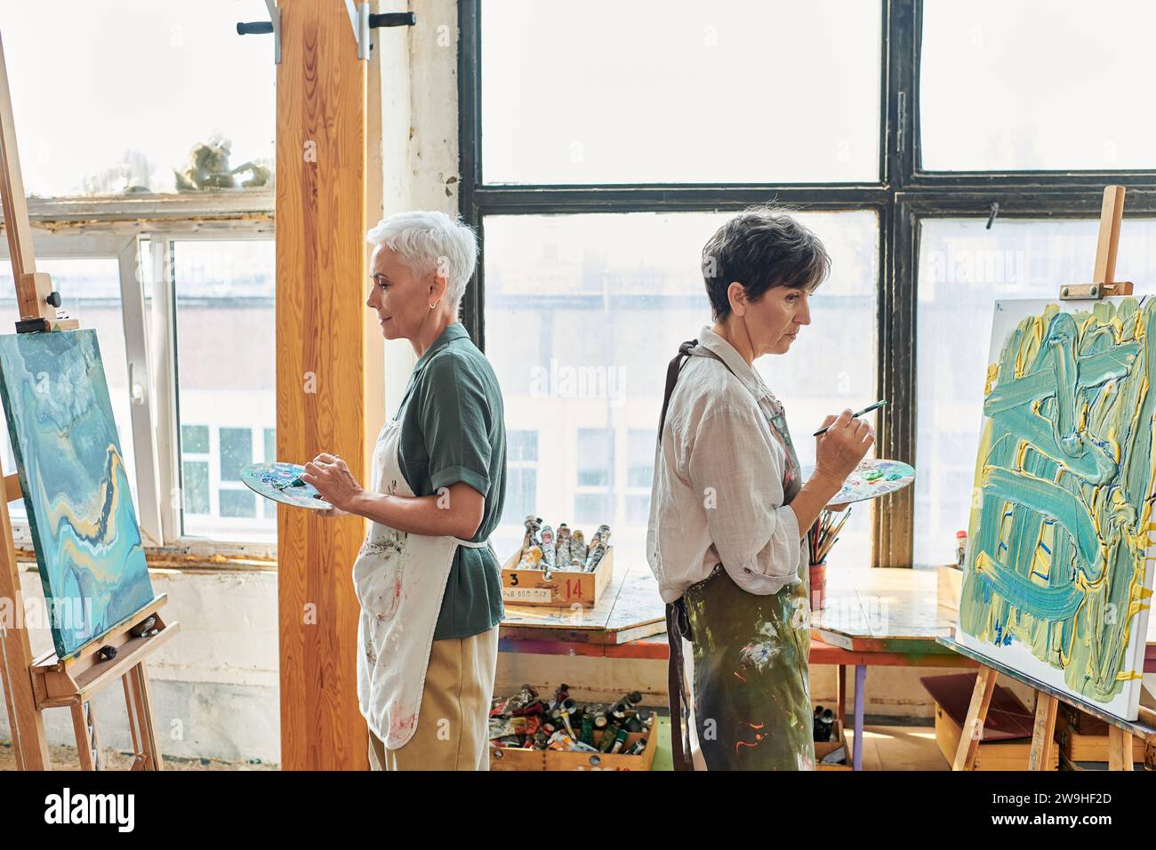 side view of mature female friends in aprons painting on easels in art