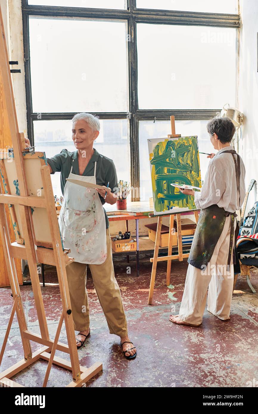 talented middle aged women in aprons painting on easels in modern art