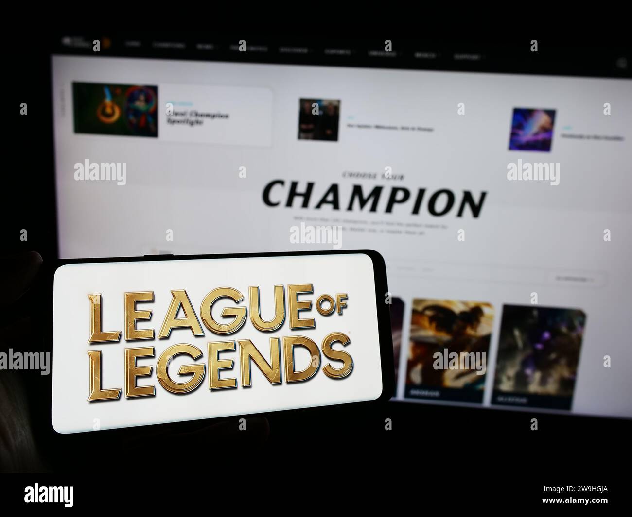 Person holding mobile phone with logo of online multiplayer video game League of Legends (LoL) in front of web page. Focus on phone display. Stock Photo