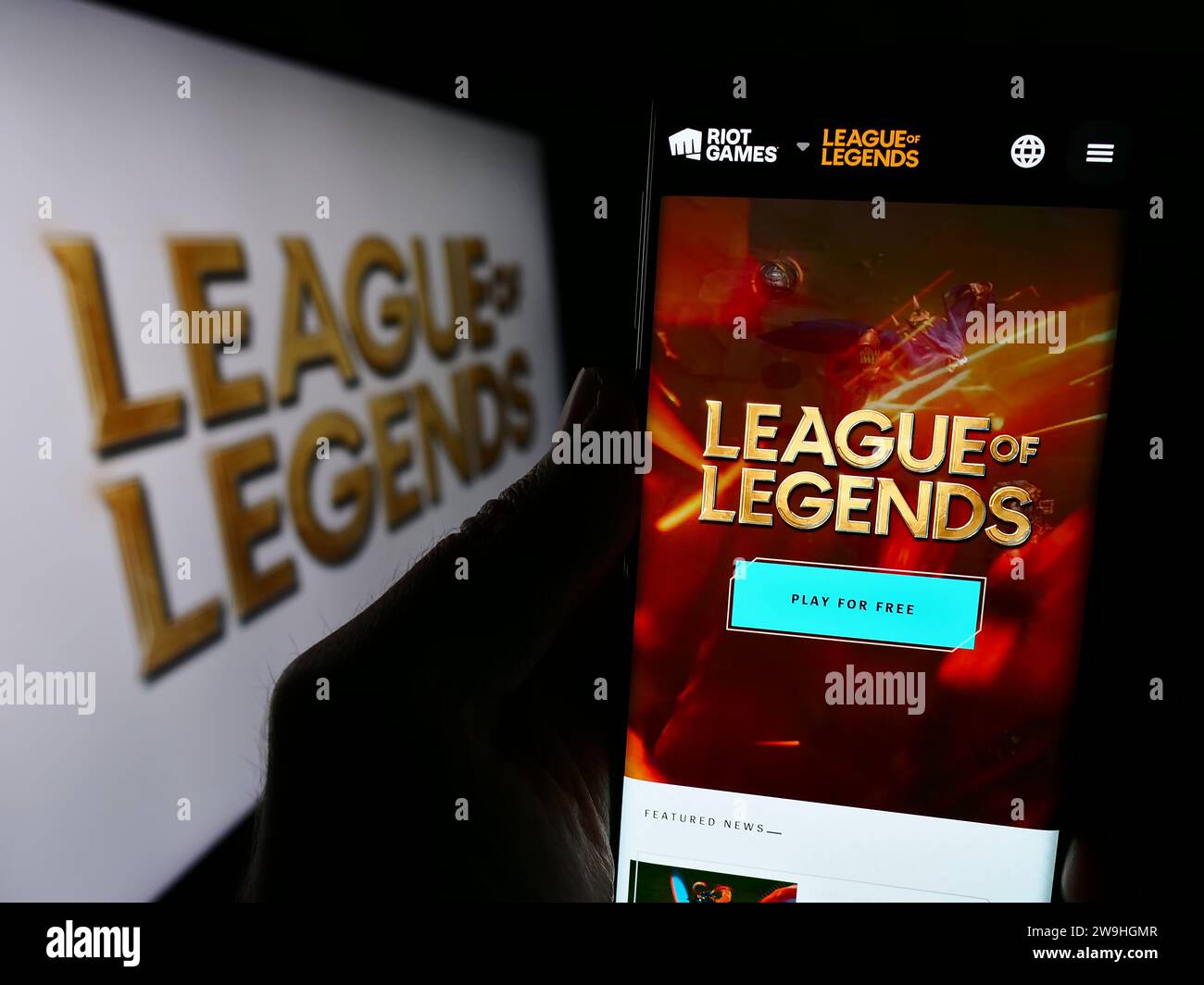 Person holding cellphone with webpage of online multiplayer video game League of Legends (LoL) in front of logo. Focus on center of phone display. Stock Photo