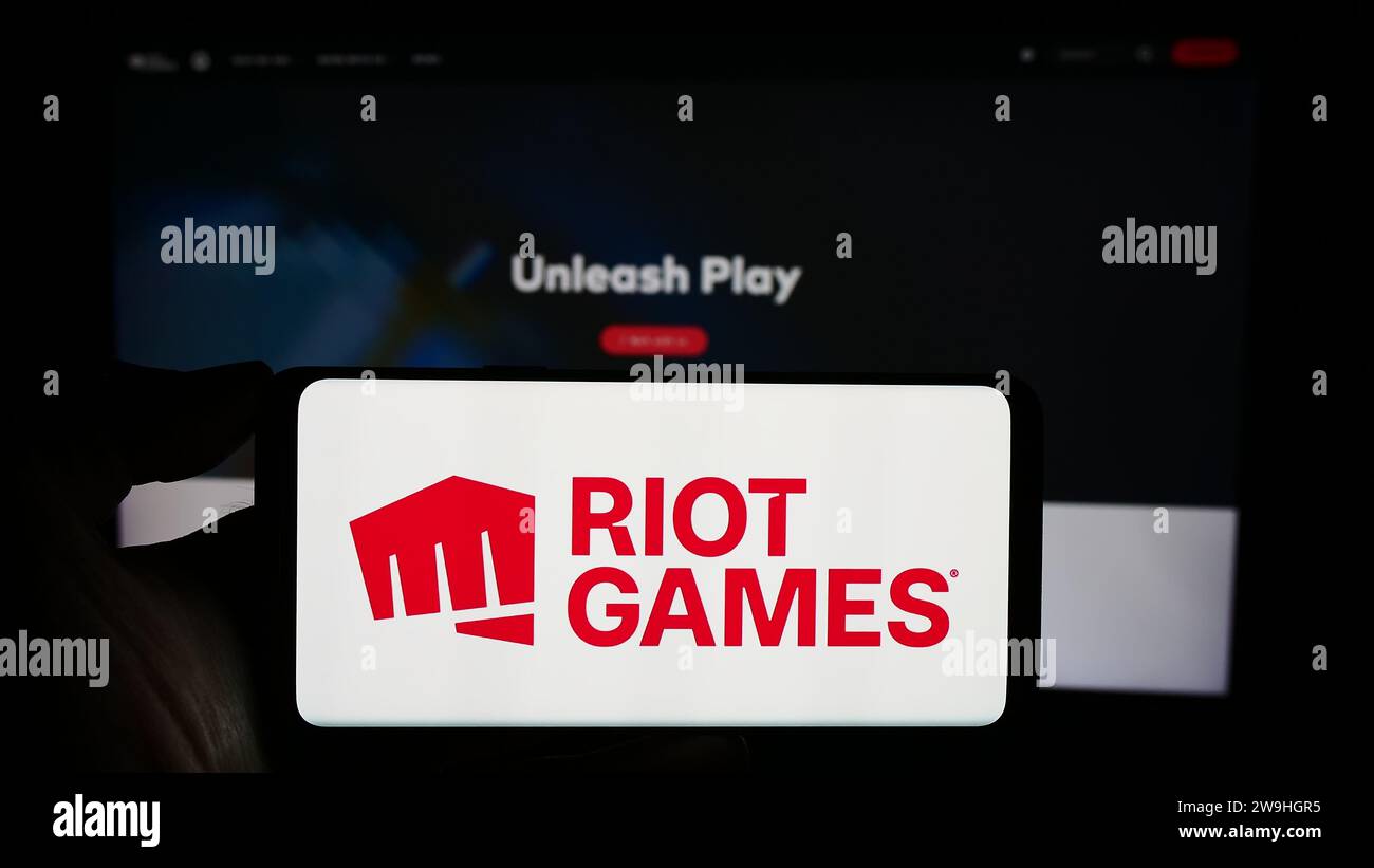 Person holding cellphone with logo of US video game development company Riot Games Inc. in front of business webpage. Focus on phone display. Stock Photo