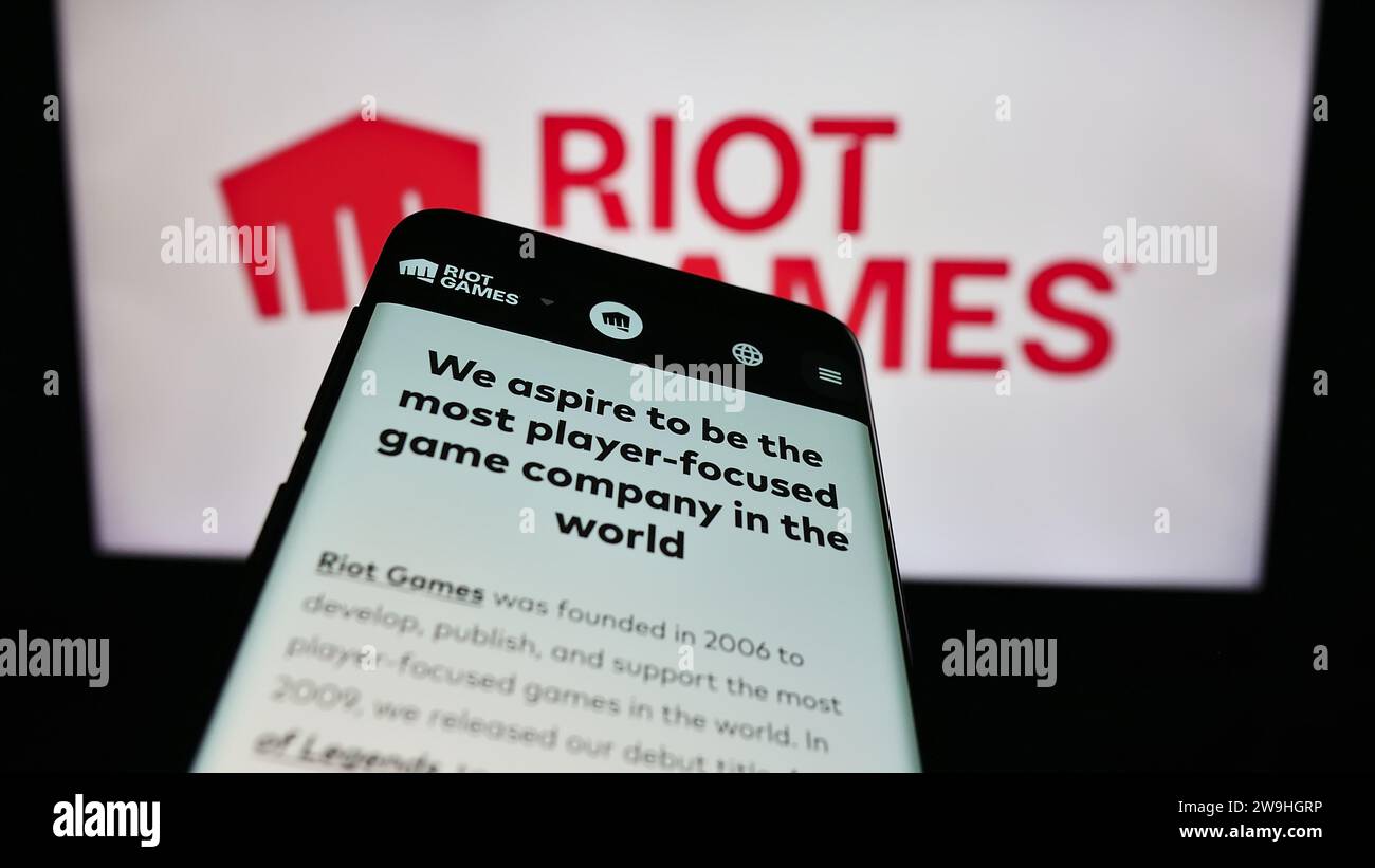 Mobile phone with website of US video game development company Riot Games Inc. in front of business logo. Focus on top-left of phone display. Stock Photo