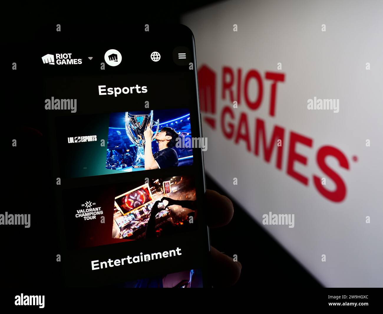 Person holding cellphone with web page of US video game development company Riot Games Inc. in front of logo. Focus on center of phone display. Stock Photo