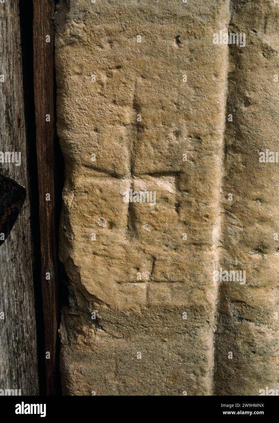 A 'Maltese Cross' (actually a cross pattée) carved on the E doorpost of the inner S doorway of St Andrew's Church, Hartburn, Northumberland, England. Stock Photo