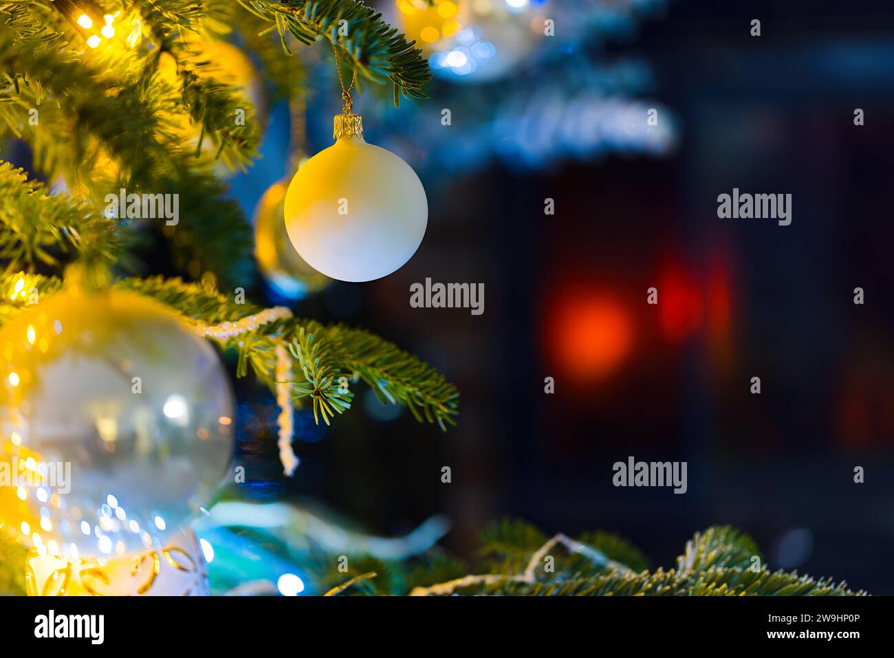 Immerse in the holiday spirit with this enchanting photo featuring baubles on a Caucasian Fir. Blurred Christmas lights and festive decor enhance the Stock Photo