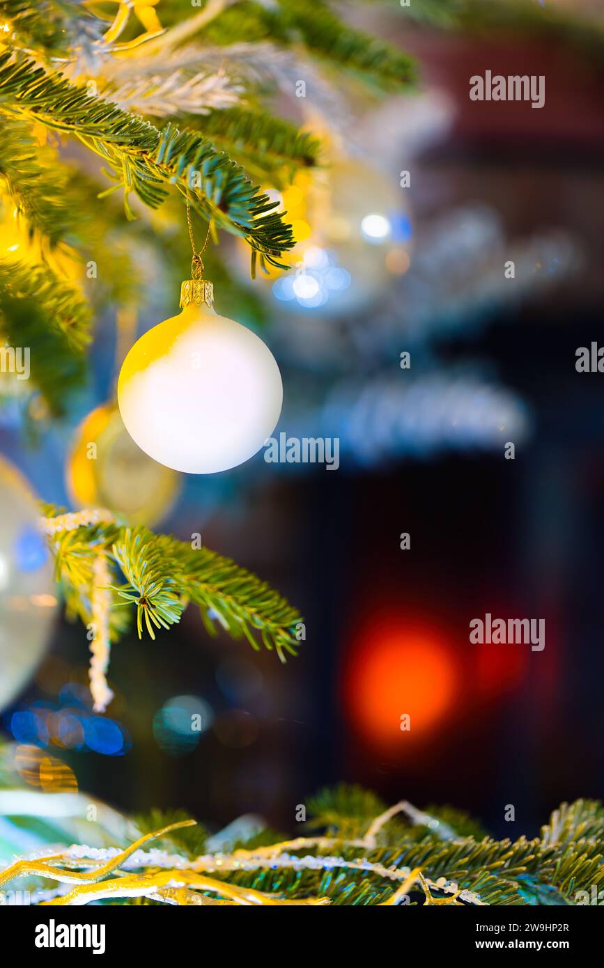 Immerse in the holiday spirit with this enchanting photo featuring baubles on a Caucasian Fir. Blurred Christmas lights and festive decor enhance the Stock Photo