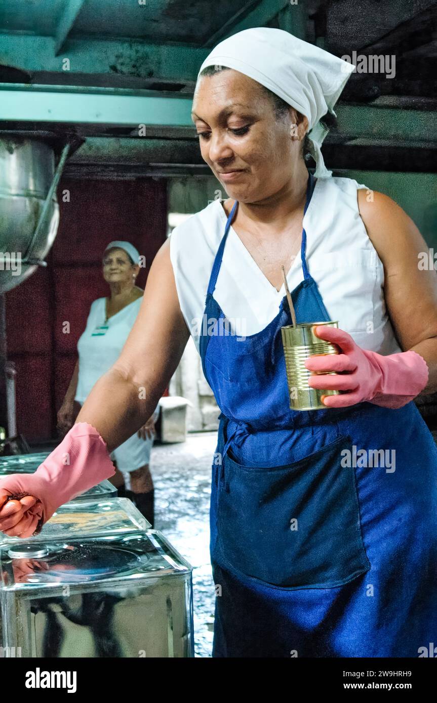 Cuban non industrial production of vegetable oil. Female worker sealing tins after filling them in a factory. Stock Photo