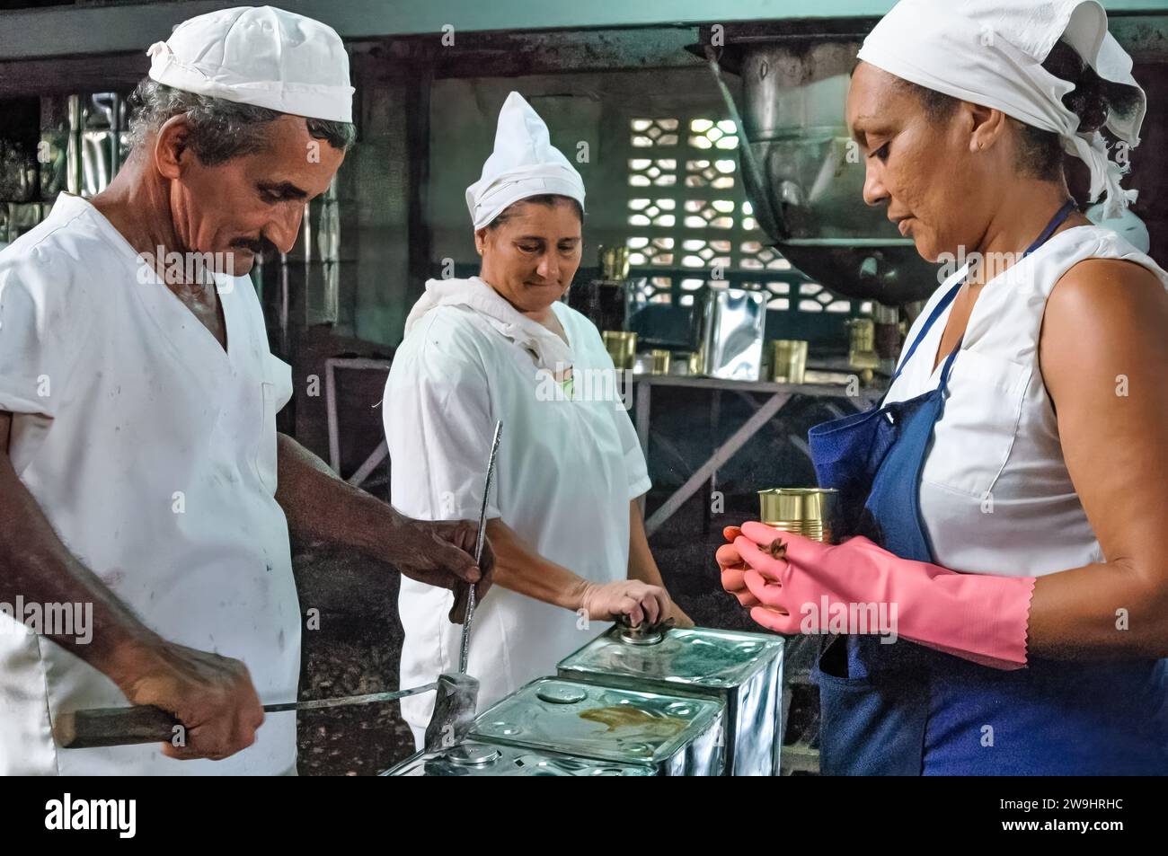 Non industrial production. Cuban male factory worker welding working on a tin canister with skewers. Other workers looking intently. Stock Photo