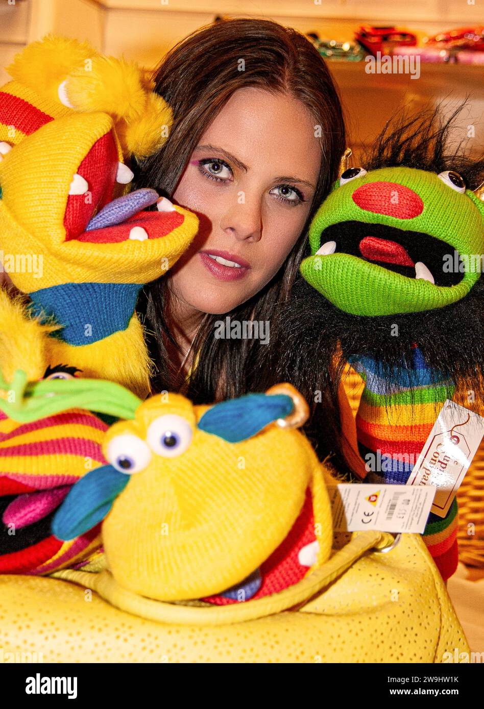 Inside a boutique store, a glamorous woman has fun modelling while playing with glove puppets in  Dundee, Scotland Stock Photo