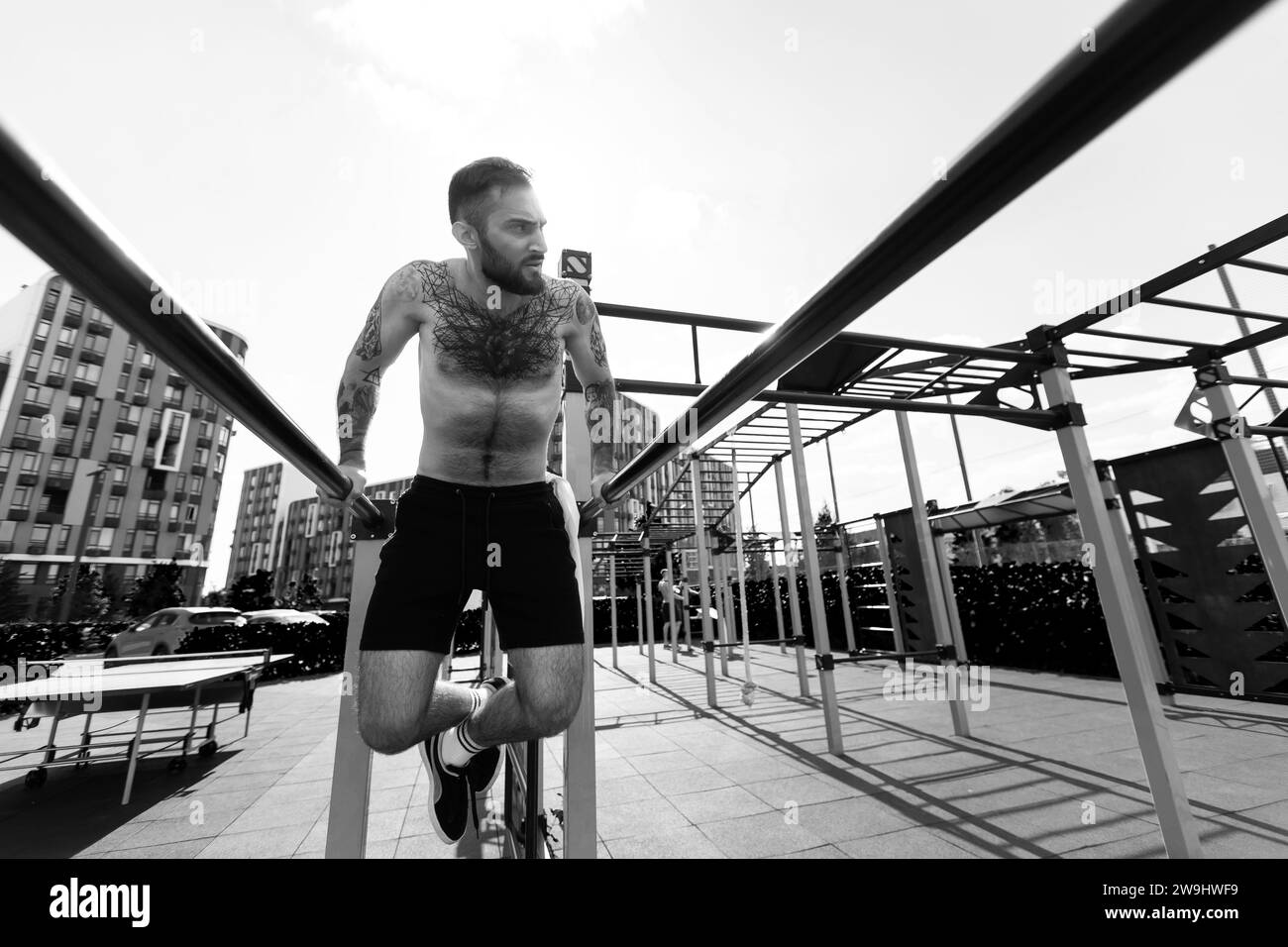 Muscular handsome man is training upper body on machines on street sports ground in city centre. Stock Photo