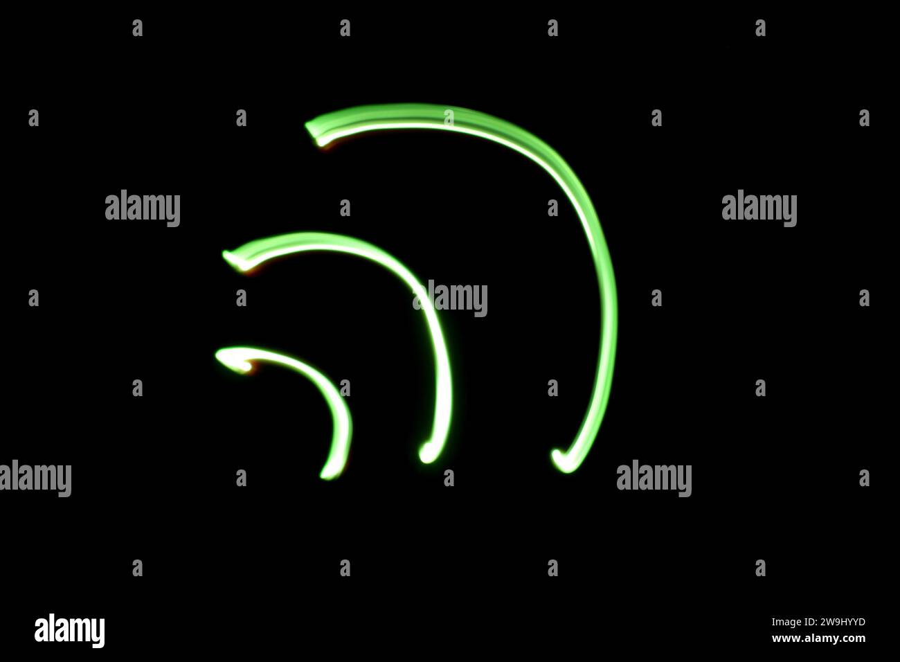 A photograph of a wireless wifi signal symbol in vibrant green light in a long exposure photo against a black background. Light painting photography Stock Photo