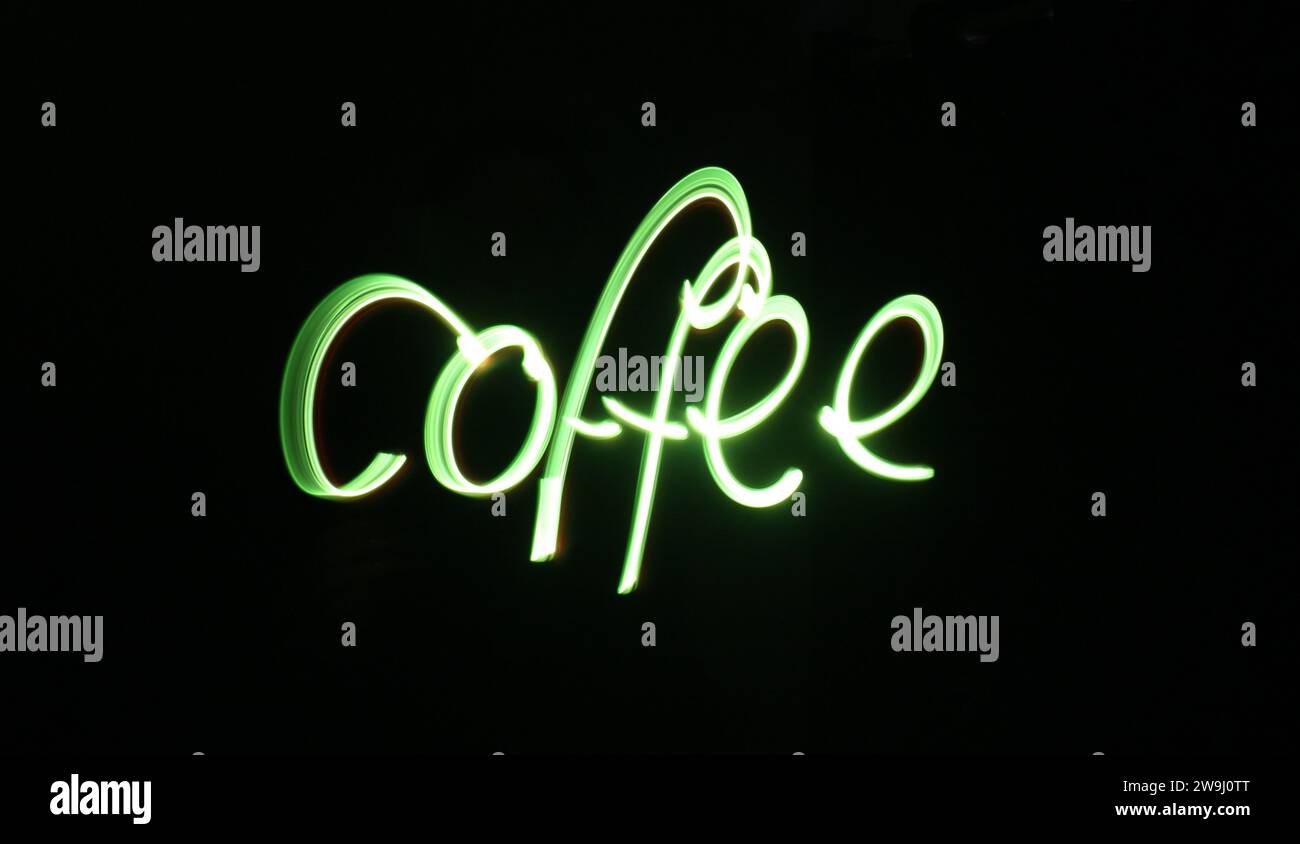 A photograph of the word 'coffee' written in vibrant green light in a long exposure photo against a black background. Light painting photography Stock Photo