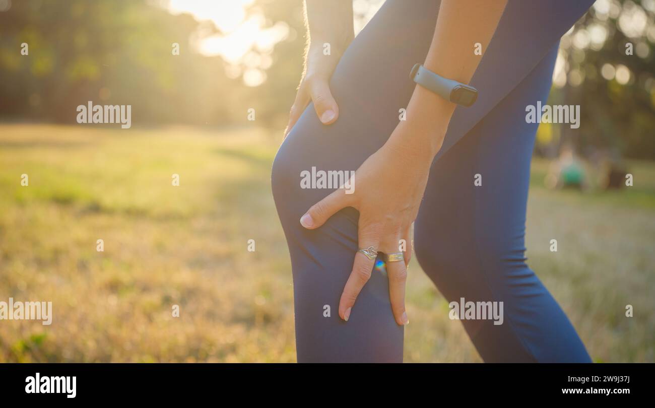 woman with knee pain in evening park. hold her sports injured knee. Low