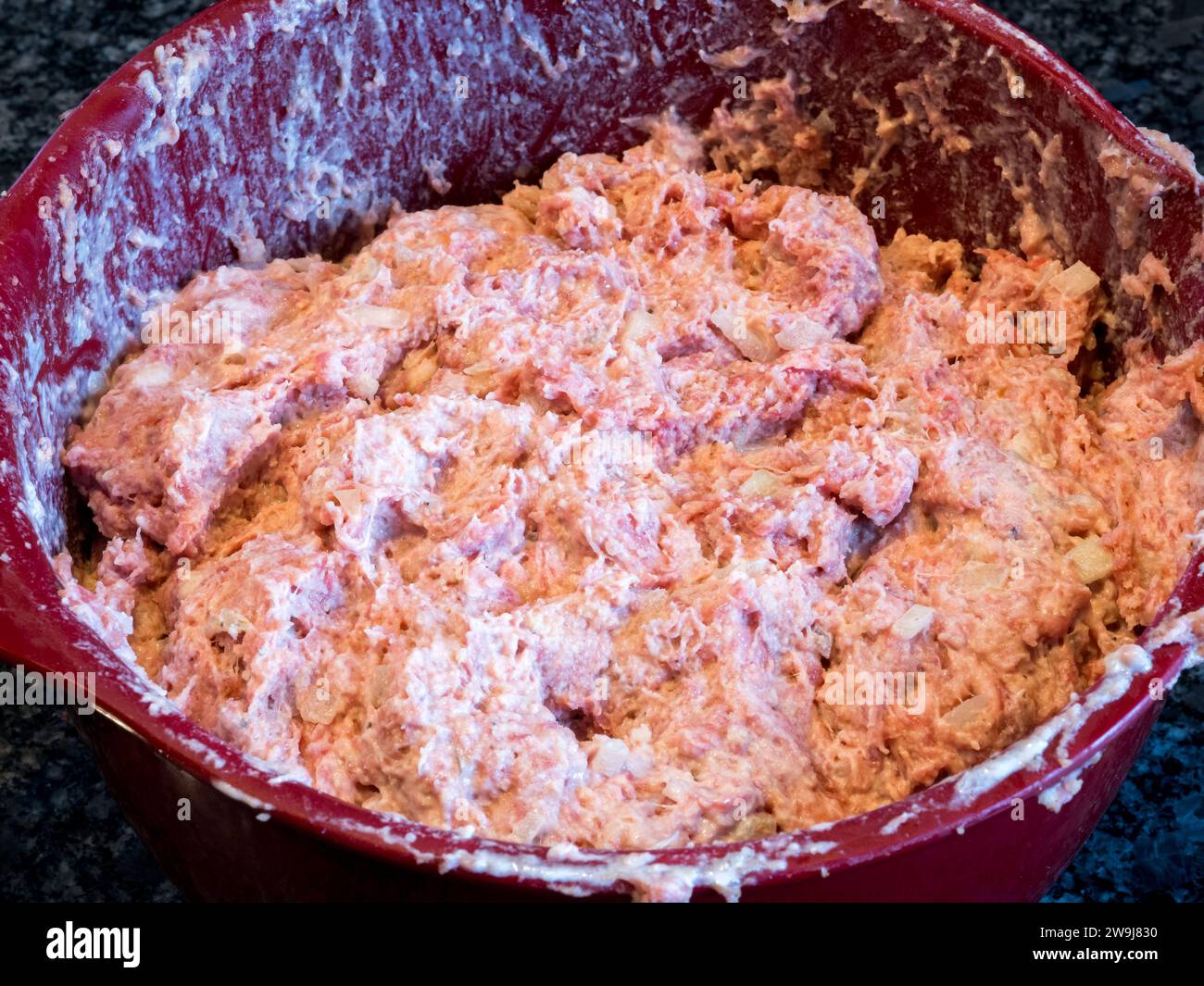 A vibrant assortment of meatball components—minced meat, onion, breadcrumbs, milk, egg, and an array of spices—rests in a scarlet bowl, awaiting the a Stock Photo