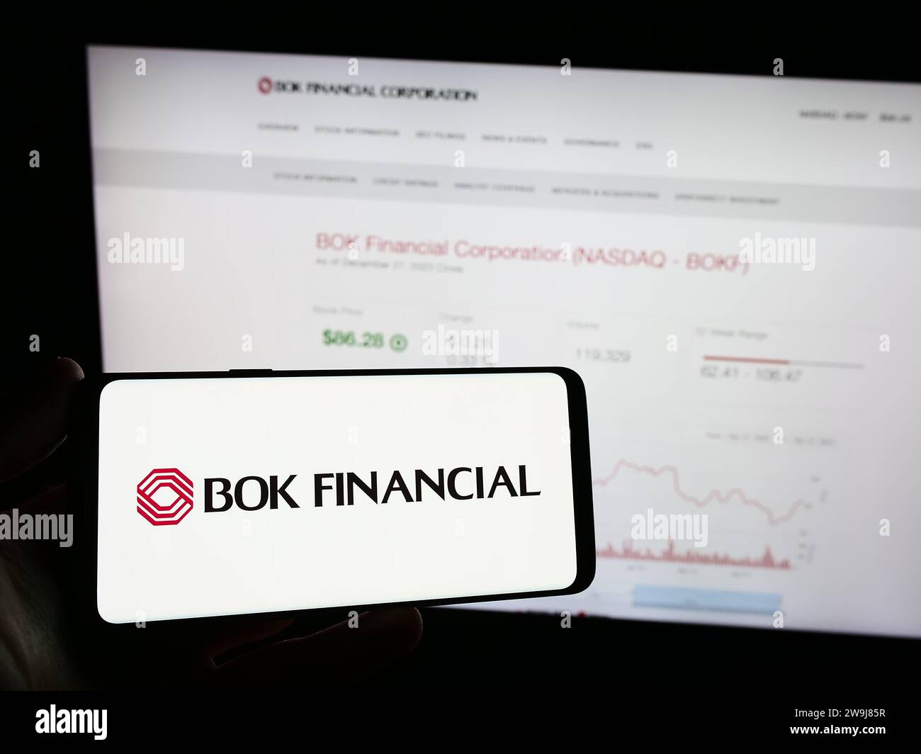 Person holding smartphone with logo of US financial services company BOK Financial Corporation in front of website. Focus on phone display. Stock Photo