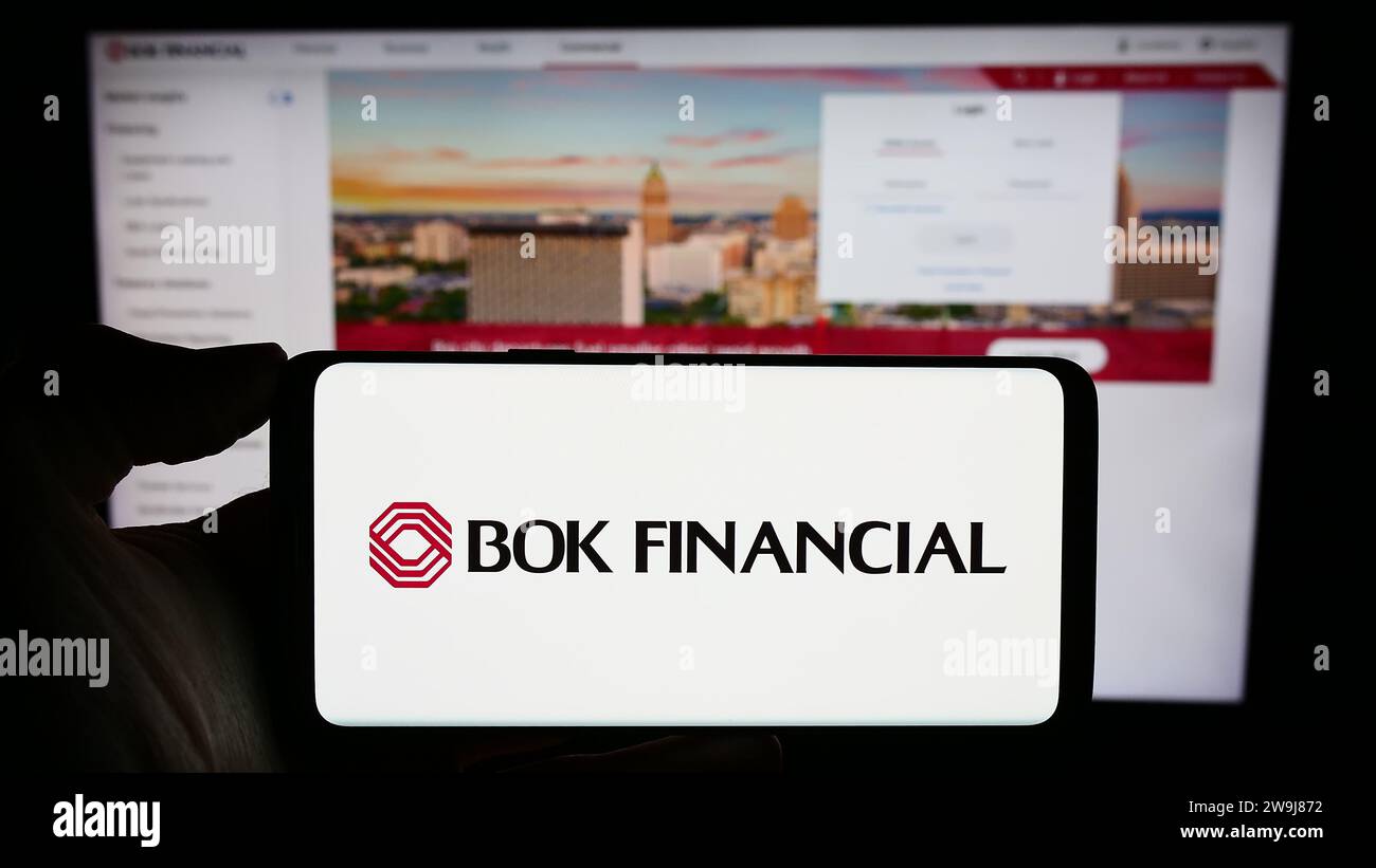 Person holding cellphone with logo of American financial services company BOK Financial Corporation in front of webpage. Focus on phone display. Stock Photo