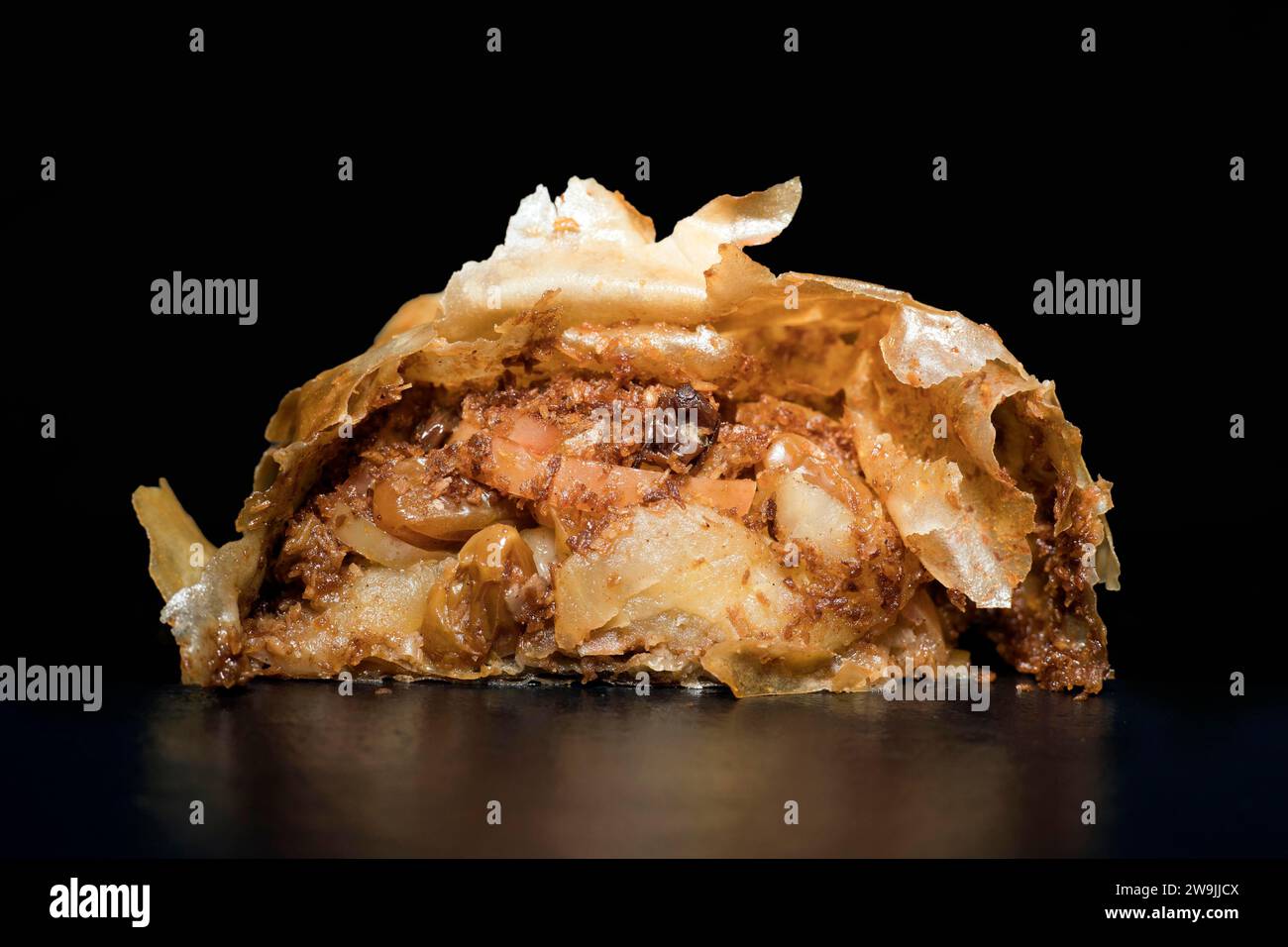Austrian apple strudel with rum sultanas, cinnamon and very thin crispy strudel dough, food photography with black background Stock Photo