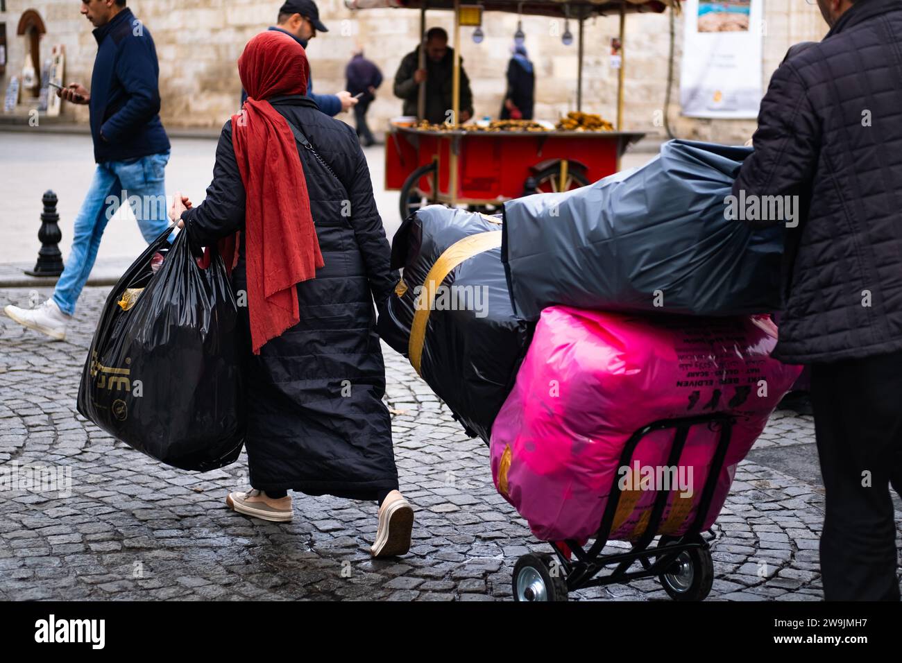Woman carrying and towing large loads in the street. A woman carries a heavy bags full of things, in hand and on trolley. Istanbul Turkey-December 20, Stock Photo