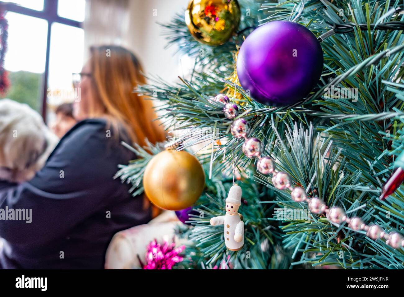 A Christmas tree decorated with coloutful baubles with a lady sat in the background Stock Photo
