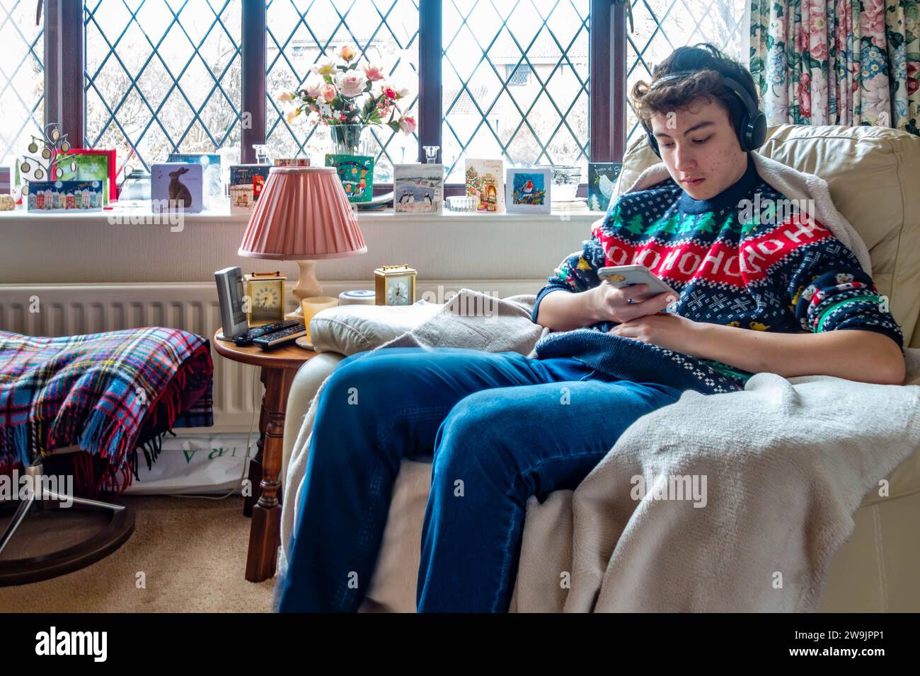 A teenage boy sits quietly listening to music stream from his phone to Bluetooth headphones on Christmas Day Stock Photo