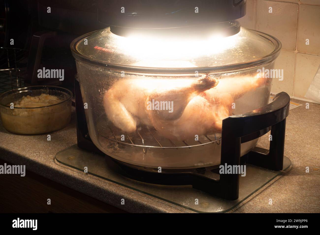 A chicken cooking in a halogen oven on a kitchen worktop Stock Photo