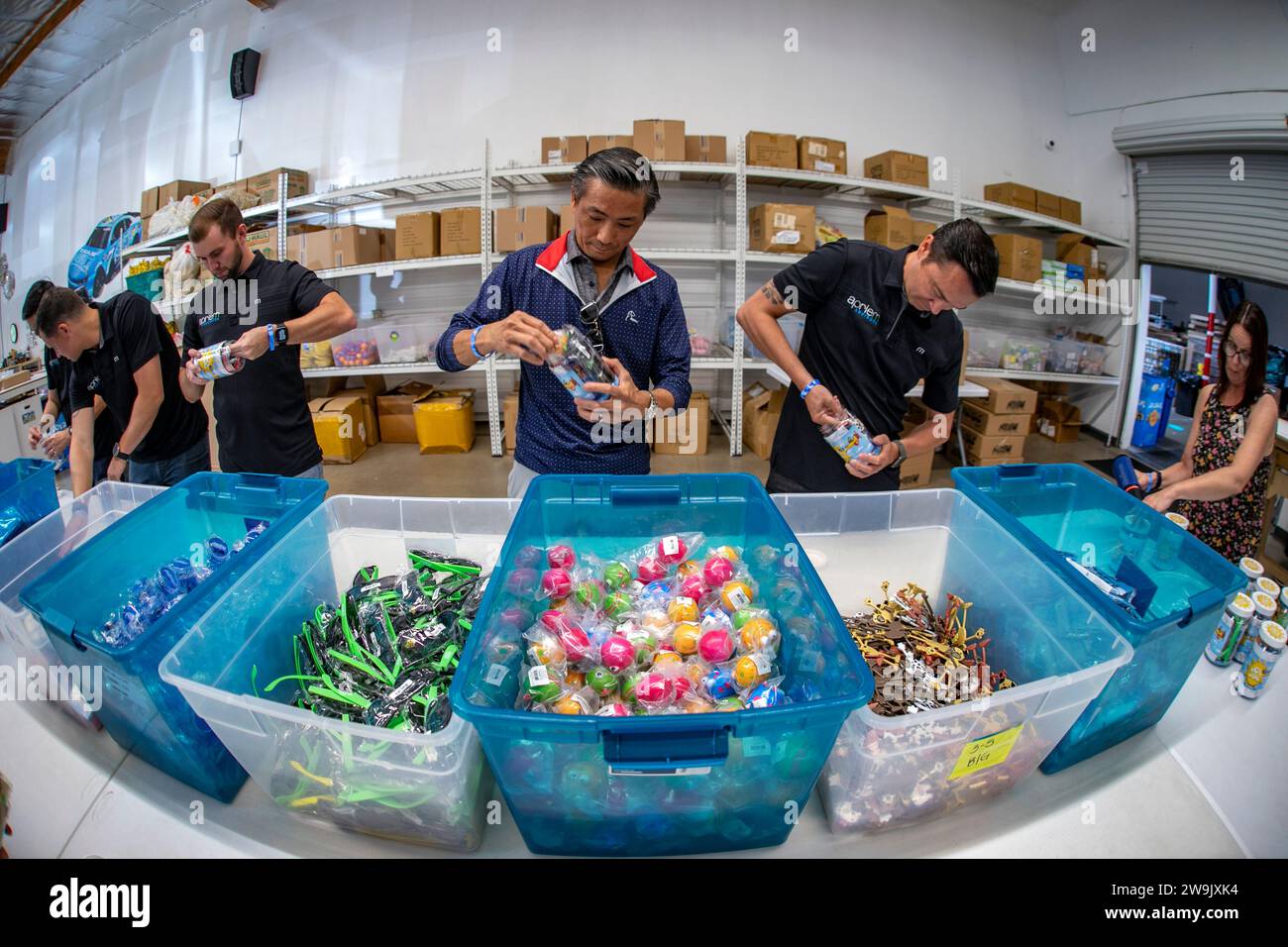 Lined up along a table with boxes full of toys, multiracial volunteers fill jars with toys for child cancer victims at the Jesse Rees Foundation in Ir Stock Photo