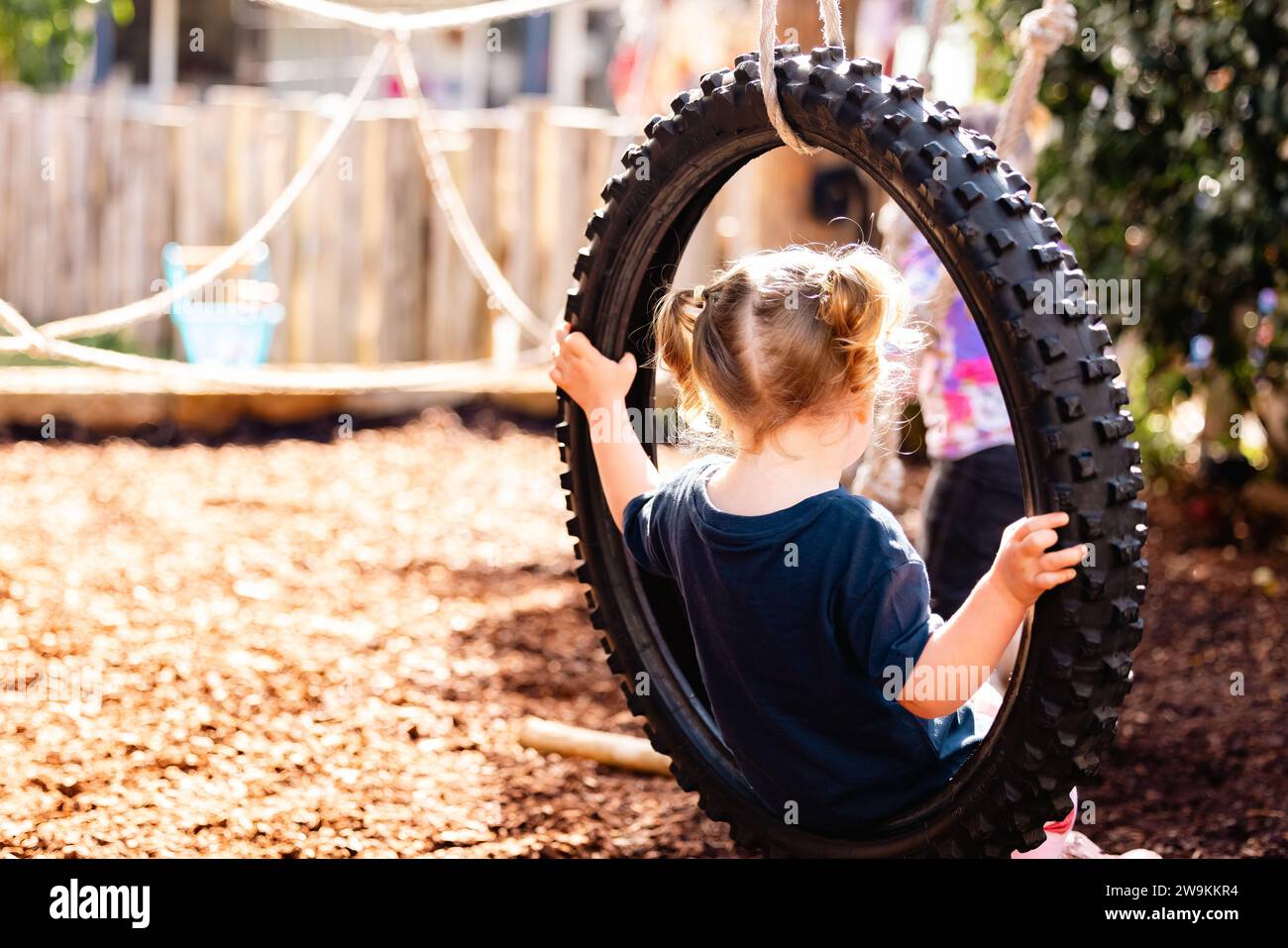 Preschool child playing on tire swing in golden morning light Stock Photo