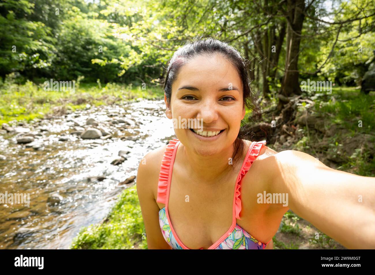 Young adult woman taking a smiling selfie in a stream in Córdoba, Argentina. She is a tourist wearing a colorful bikini. Stock Photo