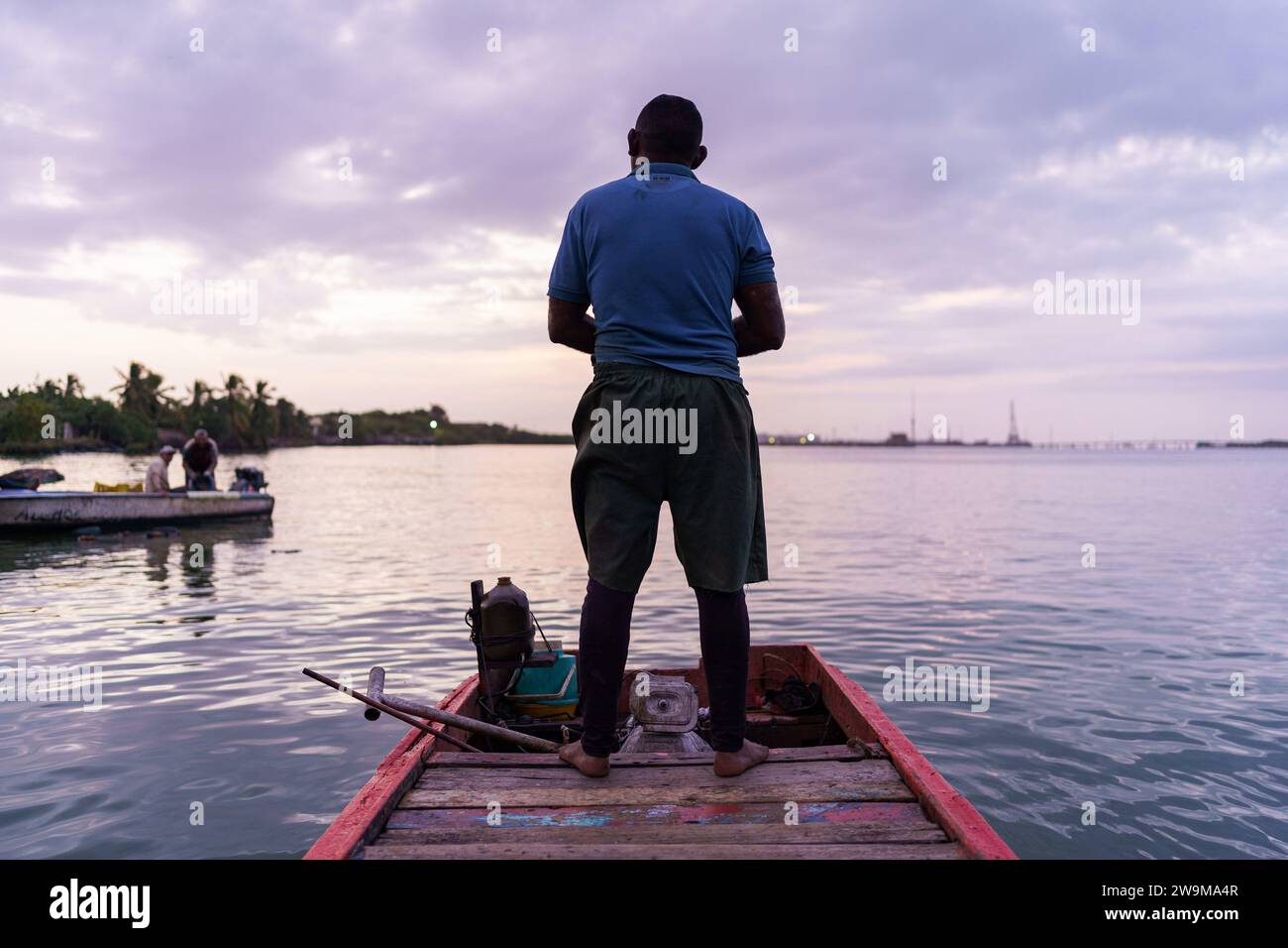 Cabimas, Venezuela. 28th Dec, 2023. A fisherman stands on his boat at sunrise while going fishing. After being exploited for intense oil extraction for decades, Lake Maracaibo has become heavily polluted due to the neglect and lack of maintainance of the old pipes and infrastructure. This has caused a severe decline in fish stock, with the appearance of bacterias and toxic algae on the water surface, damaging the lives of the people living on its shores who rely on fishing for a living. Credit: SOPA Images Limited/Alamy Live News Stock Photo