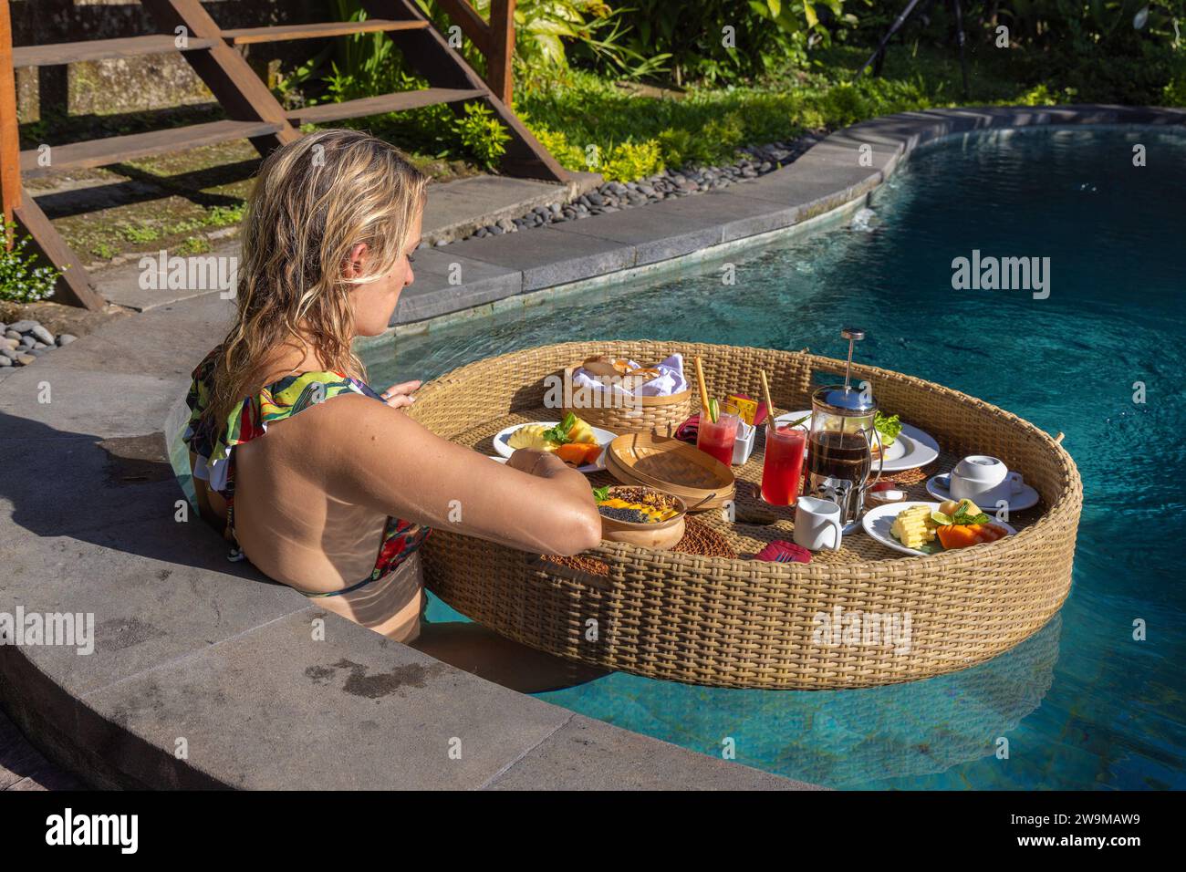A young woman having breakfast on a floating basket in a swimming pool