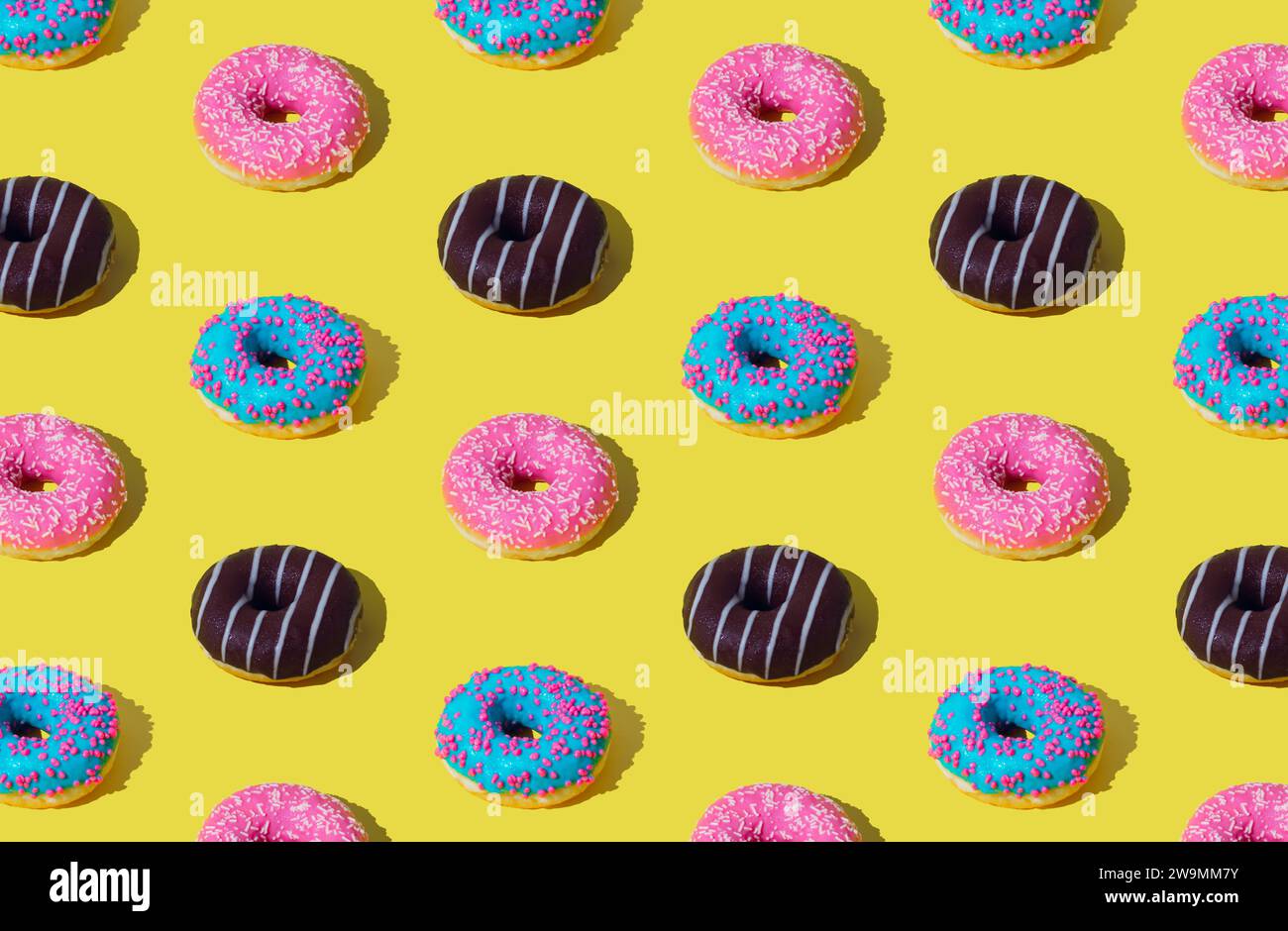 Creative pattern of colorful donuts on light yellow background. Minimal concept. Trendy donuts pattern background. Yummy food composition. Stock Photo