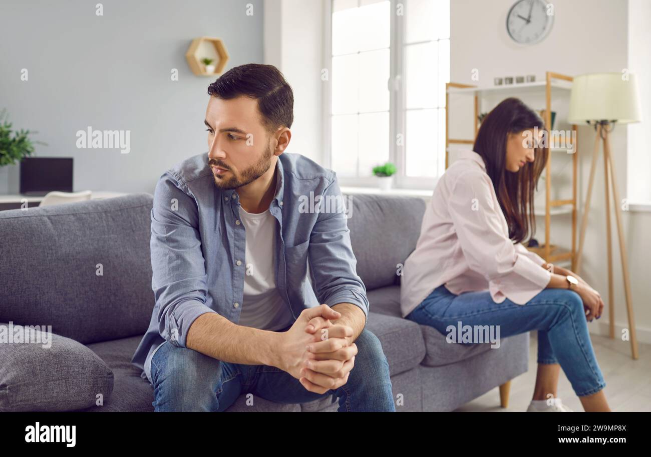 Disappointed couple sitting on sofa back to back, facing away from each other Stock Photo