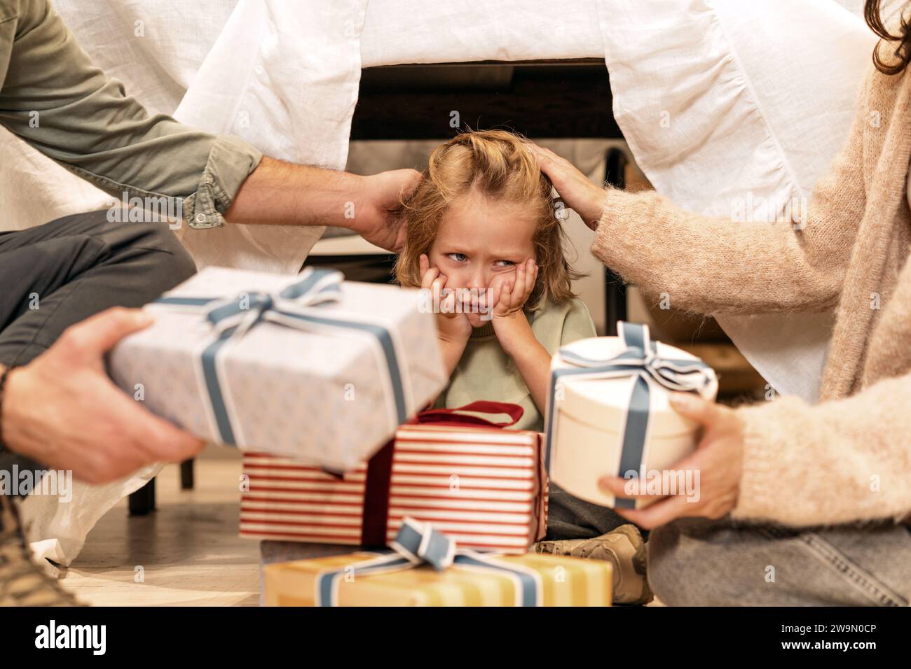 Two Parents sitting on the floor giving gifts to their unhappy son Stock Photo