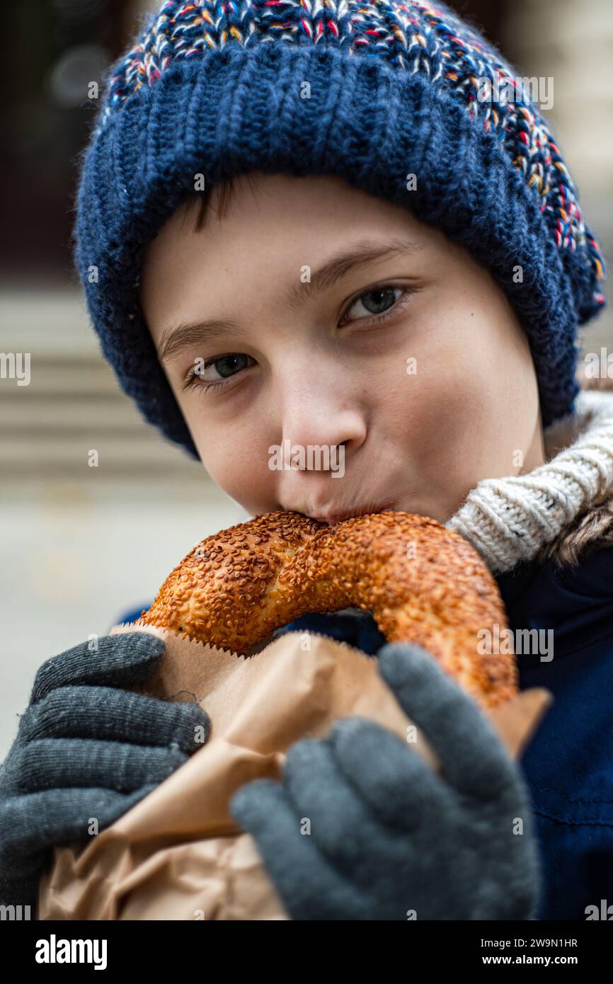 Close-up of a boy standing outdoors in warm clothing eating a sesame pastry Stock Photo