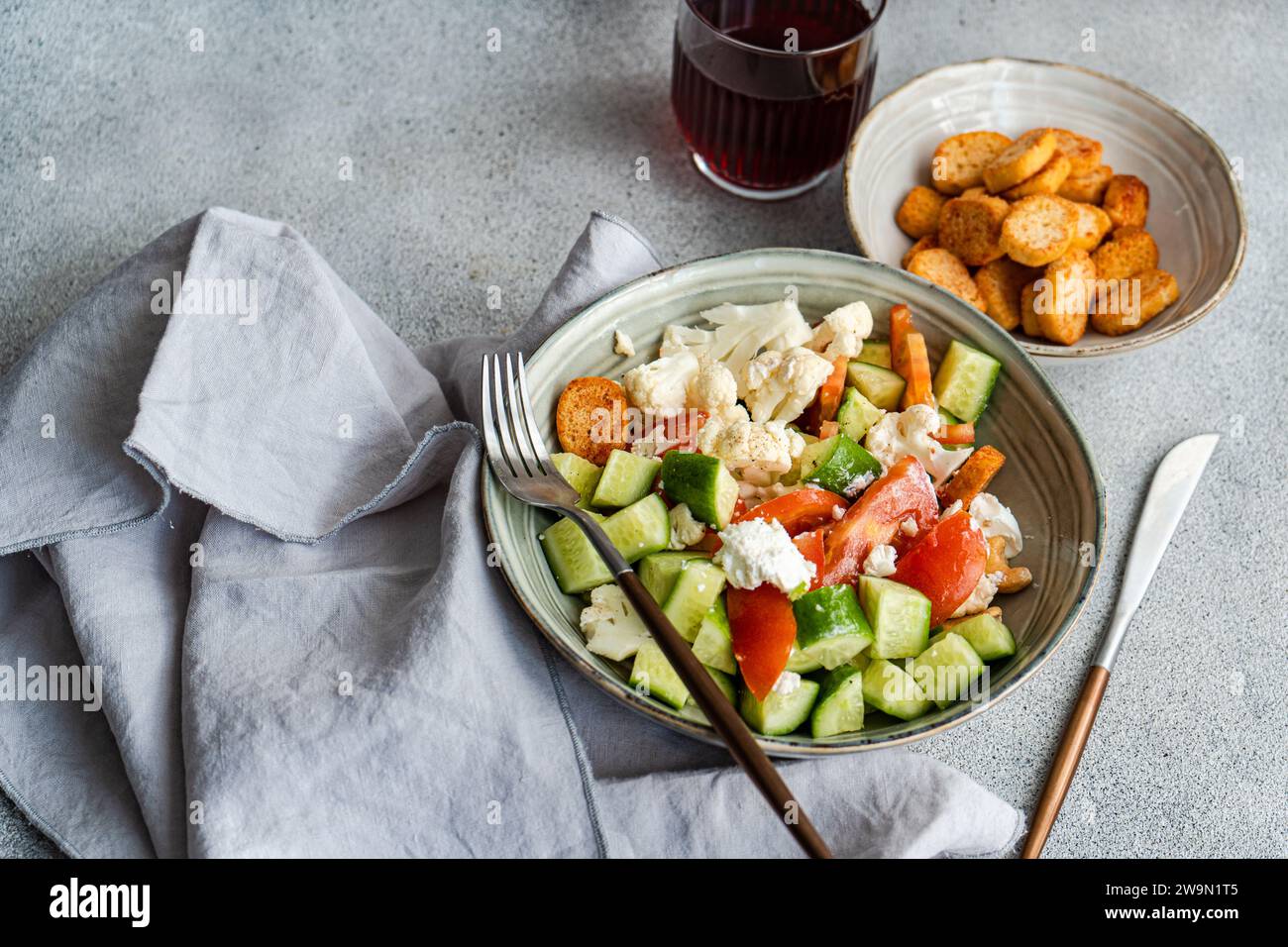 Overhead view of a bowl of tomato, cucumber, cauliflower and feta salad with croutons and a glass of cherry juice Stock Photo