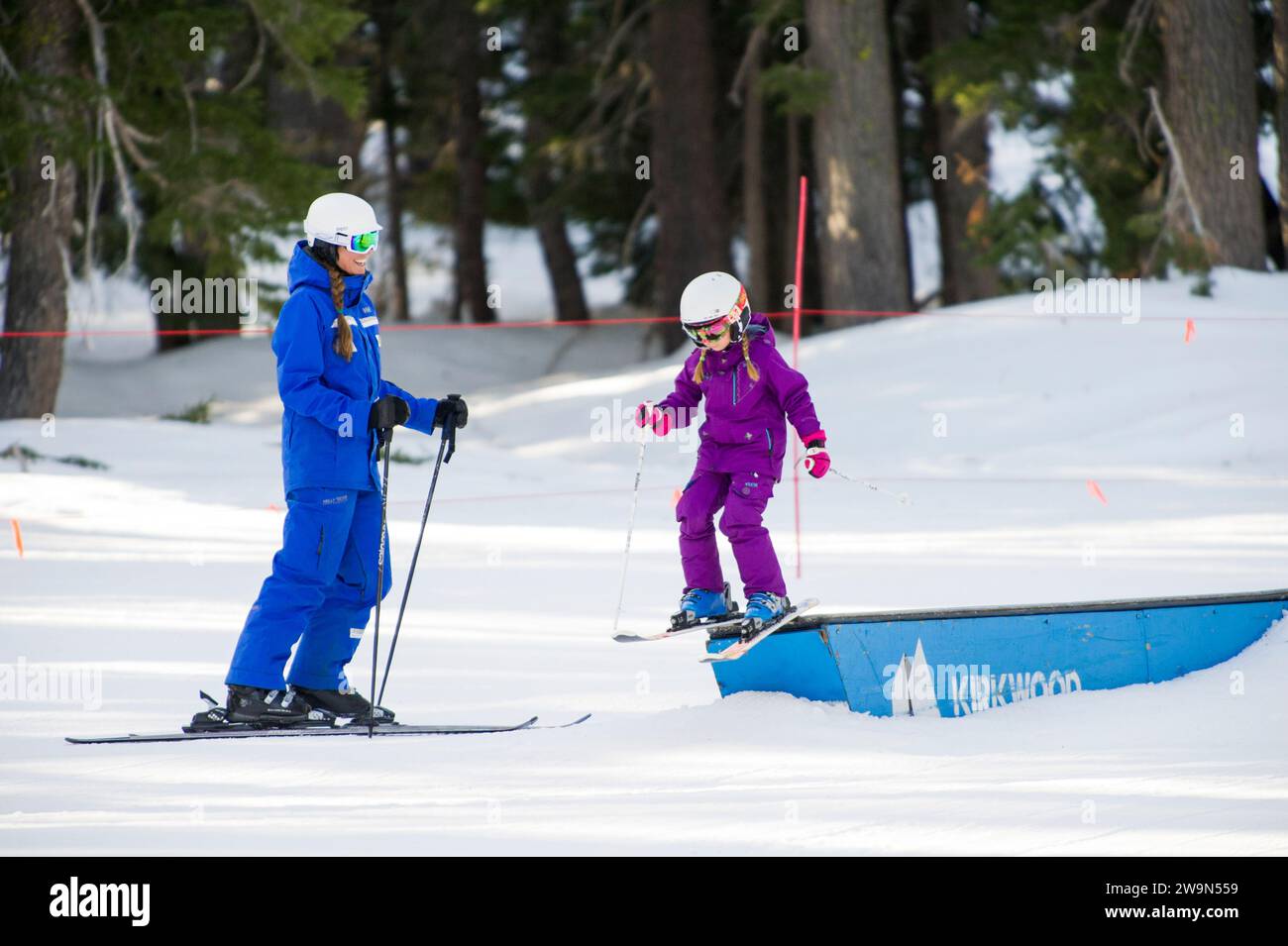A young skier jibs a box in the terrain park while their ski instructor looks on during a lesson at Kirkwood Mountain Resort in Kirkwood, California. Stock Photo