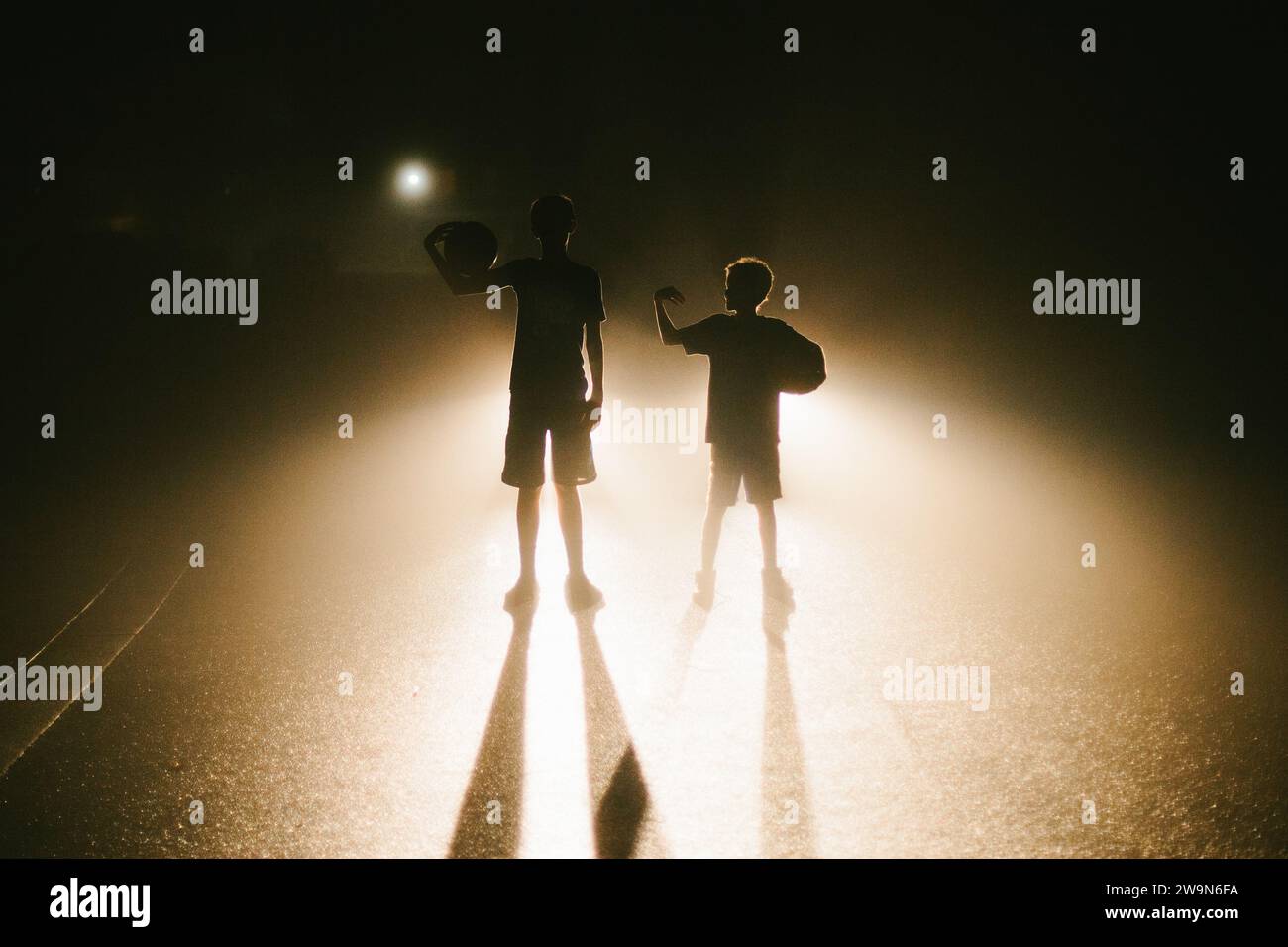 Brothers backlit at night with basketballs on the road Stock Photo