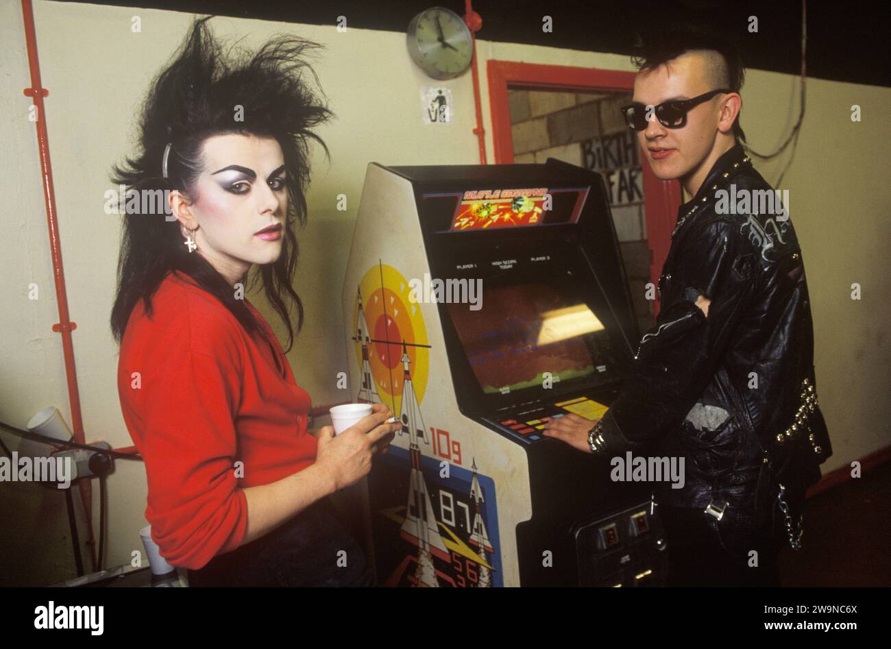 Androgynous fashion style New Romantic man 1980s young male student in makeup and 'big hair', with Punk friend in studded leather jacket playing on a Space Invader machine. College student St Martins School of Art London UK. Men wearing makeup.1985 HOMER SYKES Stock Photo