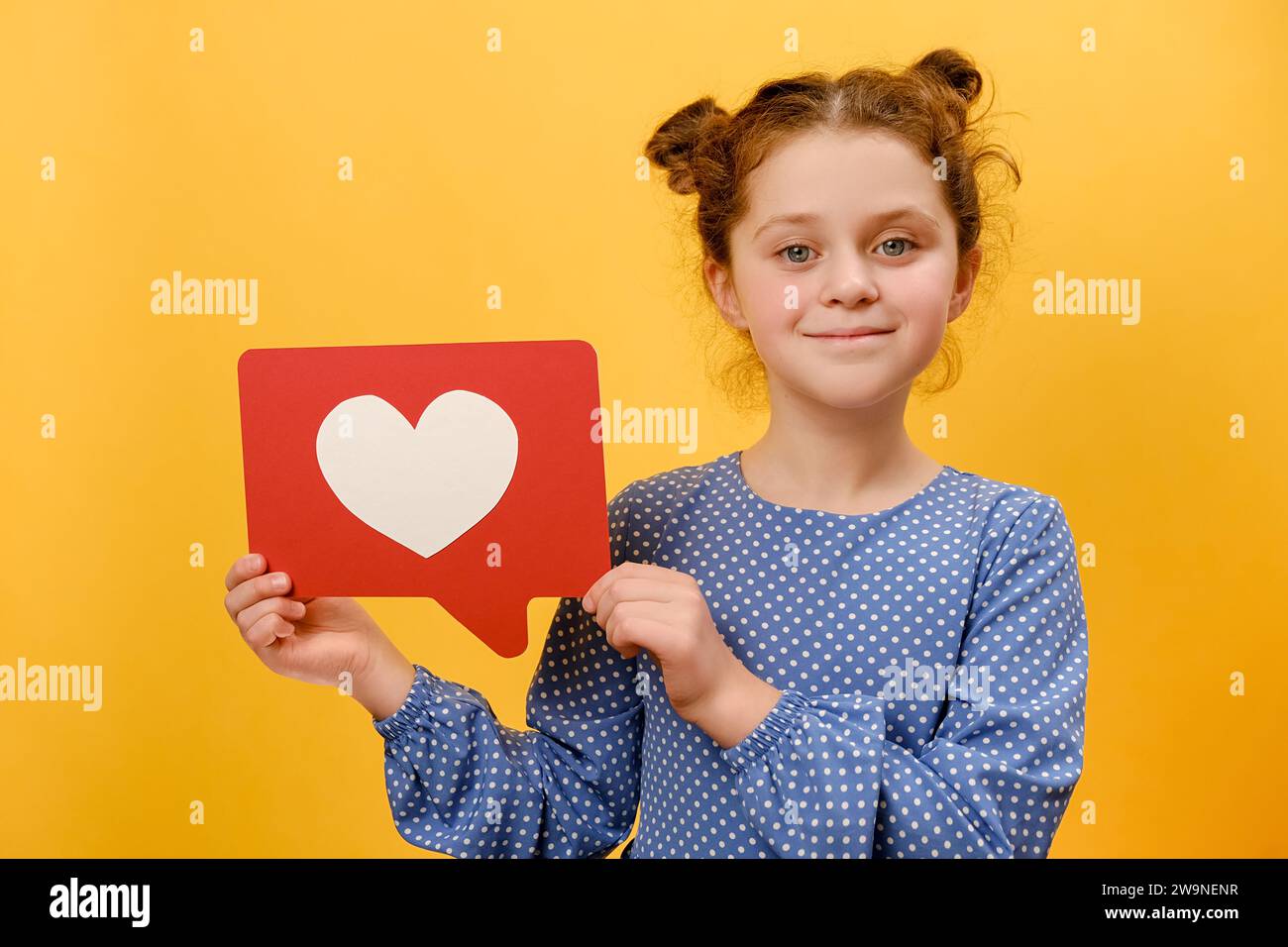 Portrait of smiling pretty little kid girl 7-8 years old holding huge like sign from social network heart form, posing isolated on yellow color backgr Stock Photo