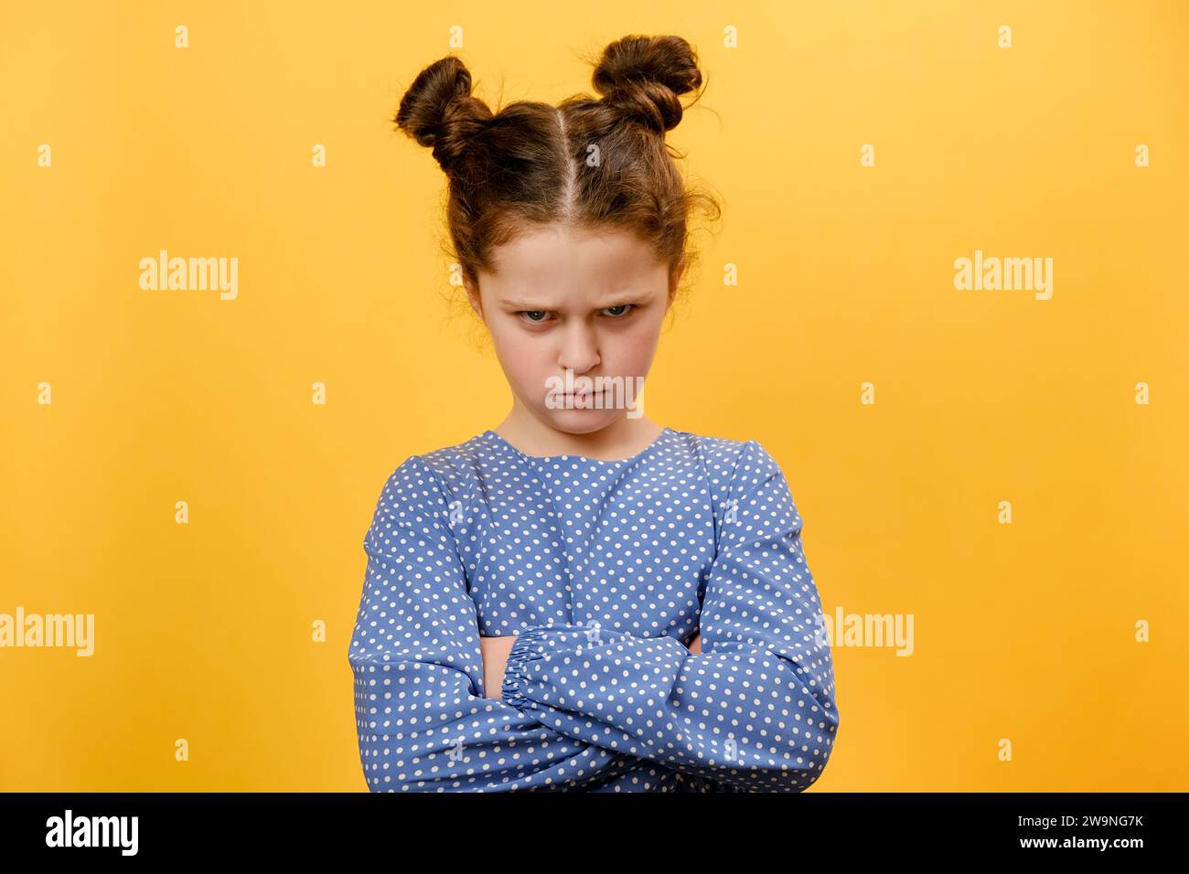 Portrait of grumpy preteen girl child pouting lips, grimacing and looking angrily at camera, posing isolated over plain yellow color background wall i Stock Photo