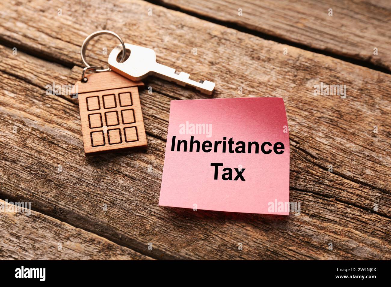 Inheritance Tax. Paper note and key with key chain in shape of house on wooden table, closeup Stock Photo