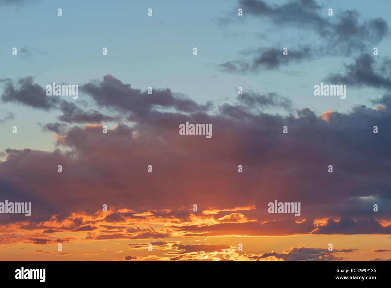 A stunning sunset sky painted with fiery orange clouds and a soft blue ...