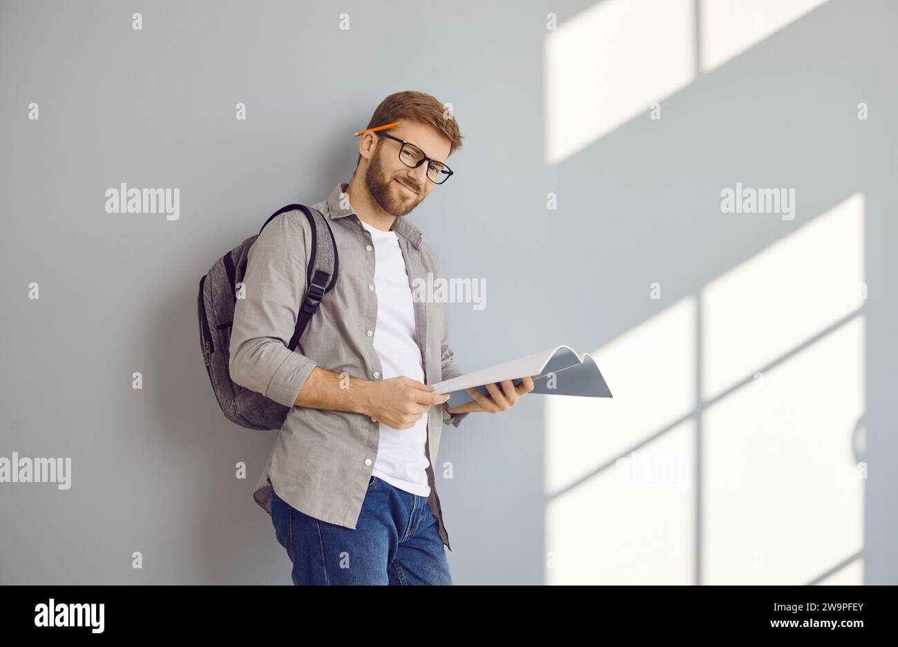Portrait of happy male student with textbook and backpack standing by ...