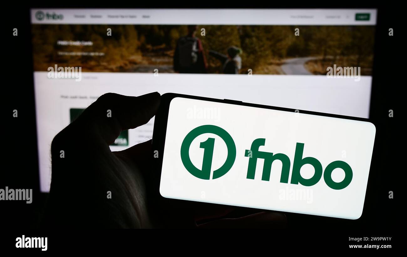 Person holding mobile phone with logo of American financial company First National Bank Omaha (FNBO) in front of web page. Focus on phone display. Stock Photo