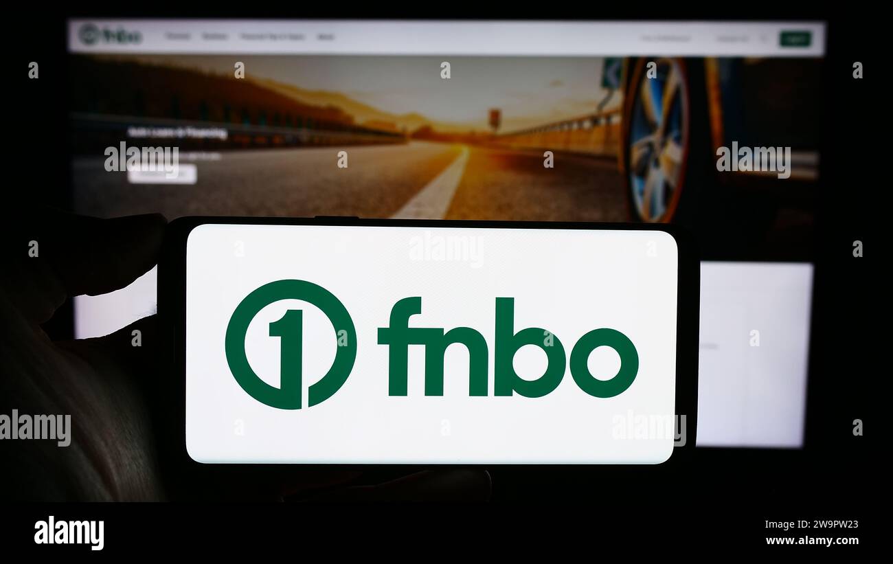 Person holding cellphone with logo of US financial company First National Bank Omaha (FNBO) in front of business webpage. Focus on phone display. Stock Photo