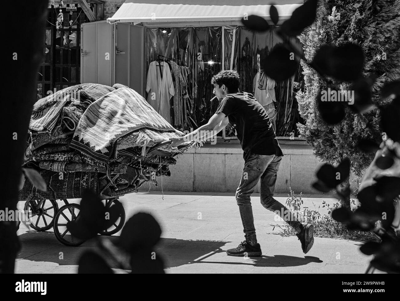 Shiraz, Iran - 06.26.2023: Iranian man, worker carry carpet by wheelbarrow. Black and white photo of iran. Stock Photo