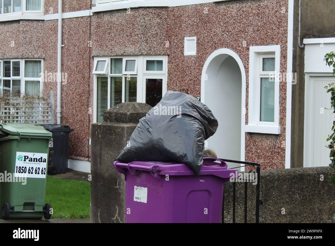 Dublin, Ireland - December 27th 2023: A photo of a full black bin bag on top of a purple compost bin out on the street. Stock Photo