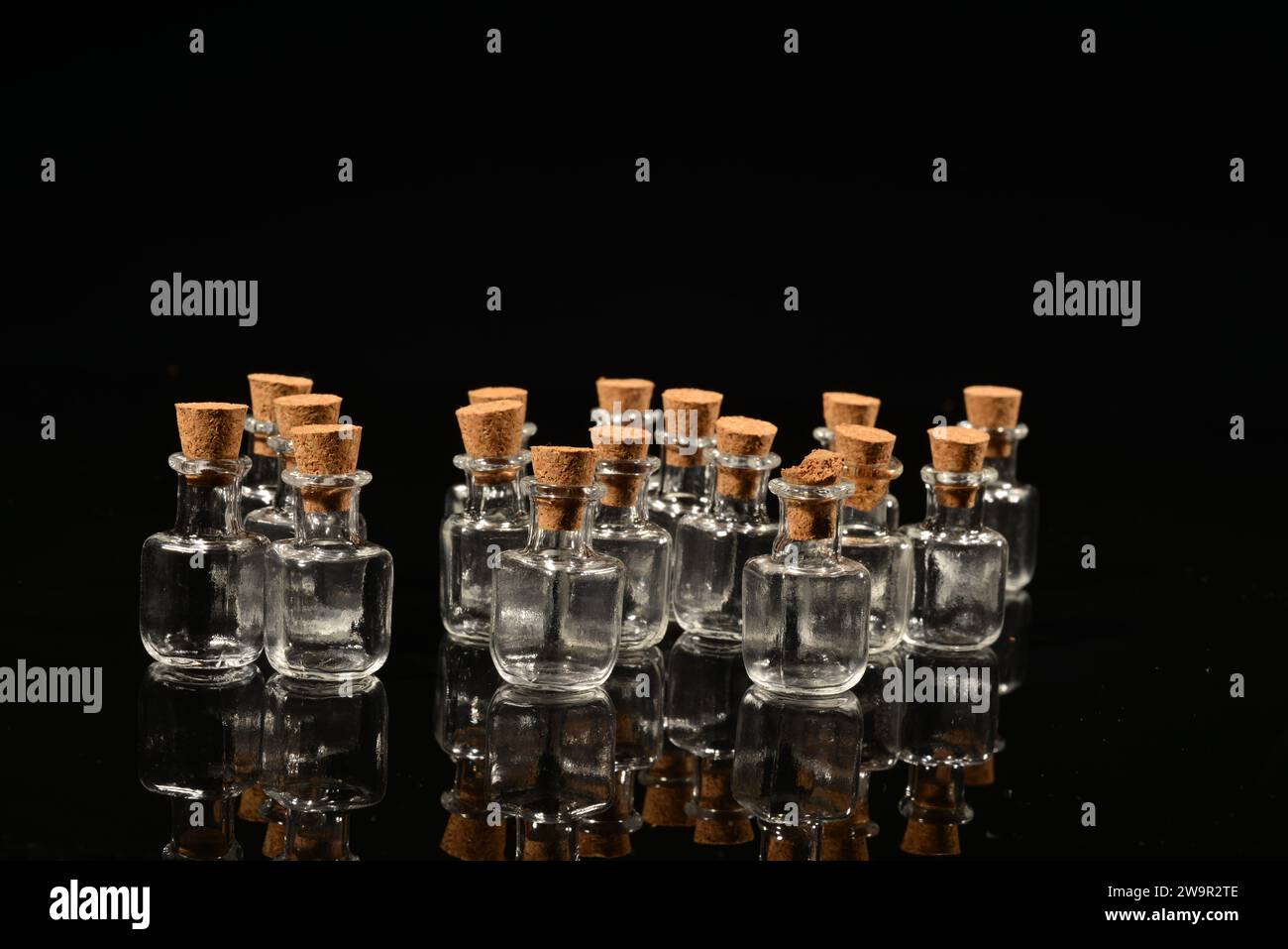 Glass bottles with cork on a black mirror surface with reflections isolated on black background. Stock Photo