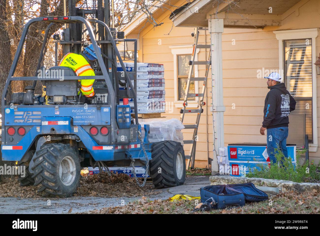 Two workers unloading asphalt roofing shingles from forklift for roof replacement Stock Photo