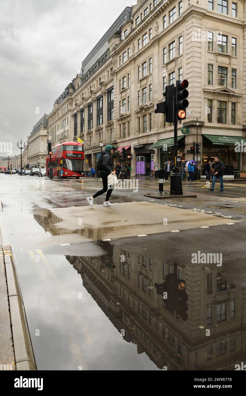 London, UK - March 17 2023; London street scene on wet day with pedestrian reflecting in puddle Stock Photo
